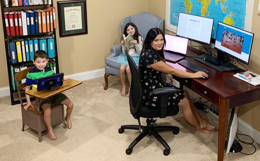 A woman working in a home office as two children sit nearby. 