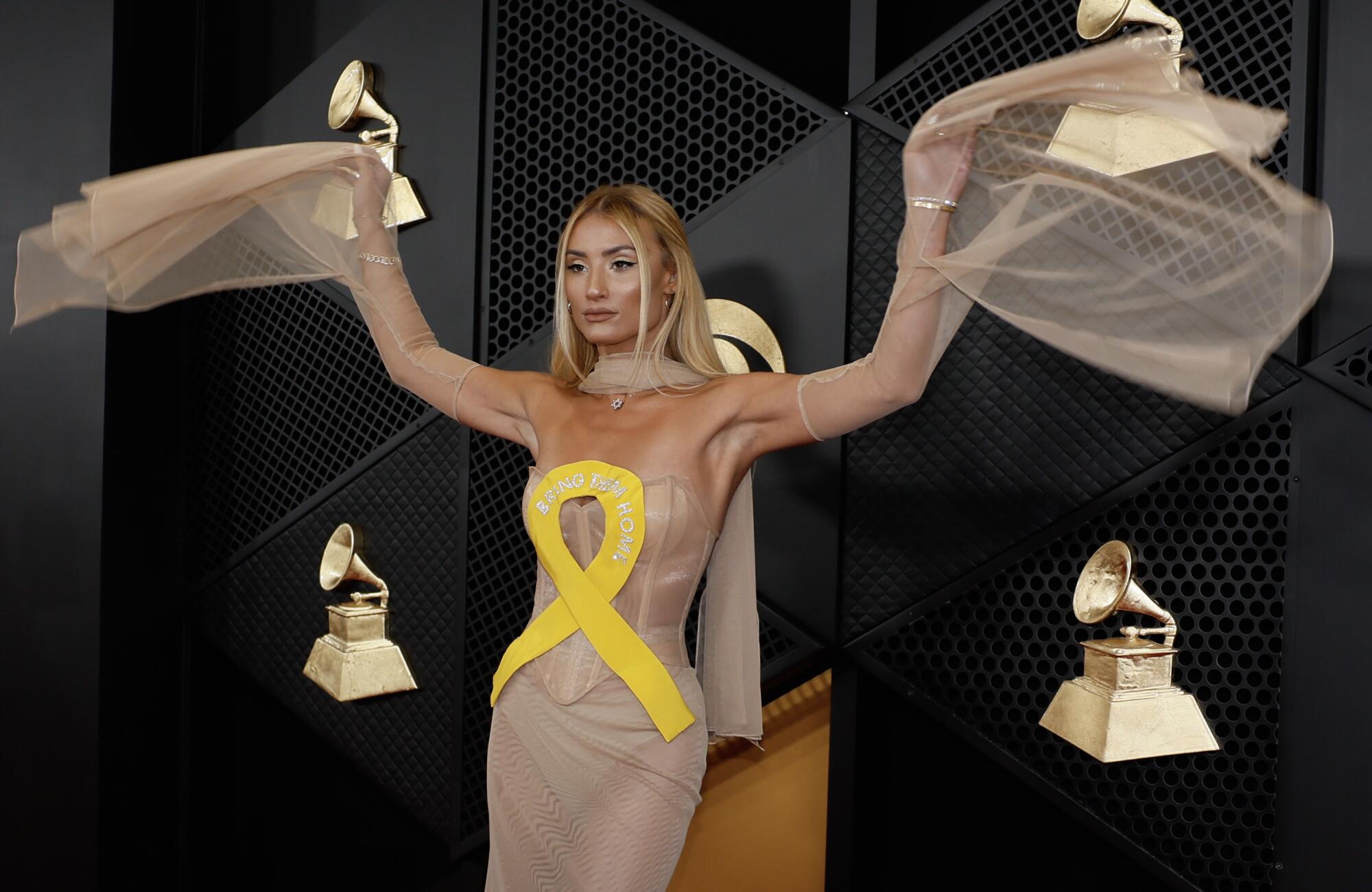 Montana Tucker, in a beige bustier dress adorned with a yellow ribbon, raises her arms on the red carpet