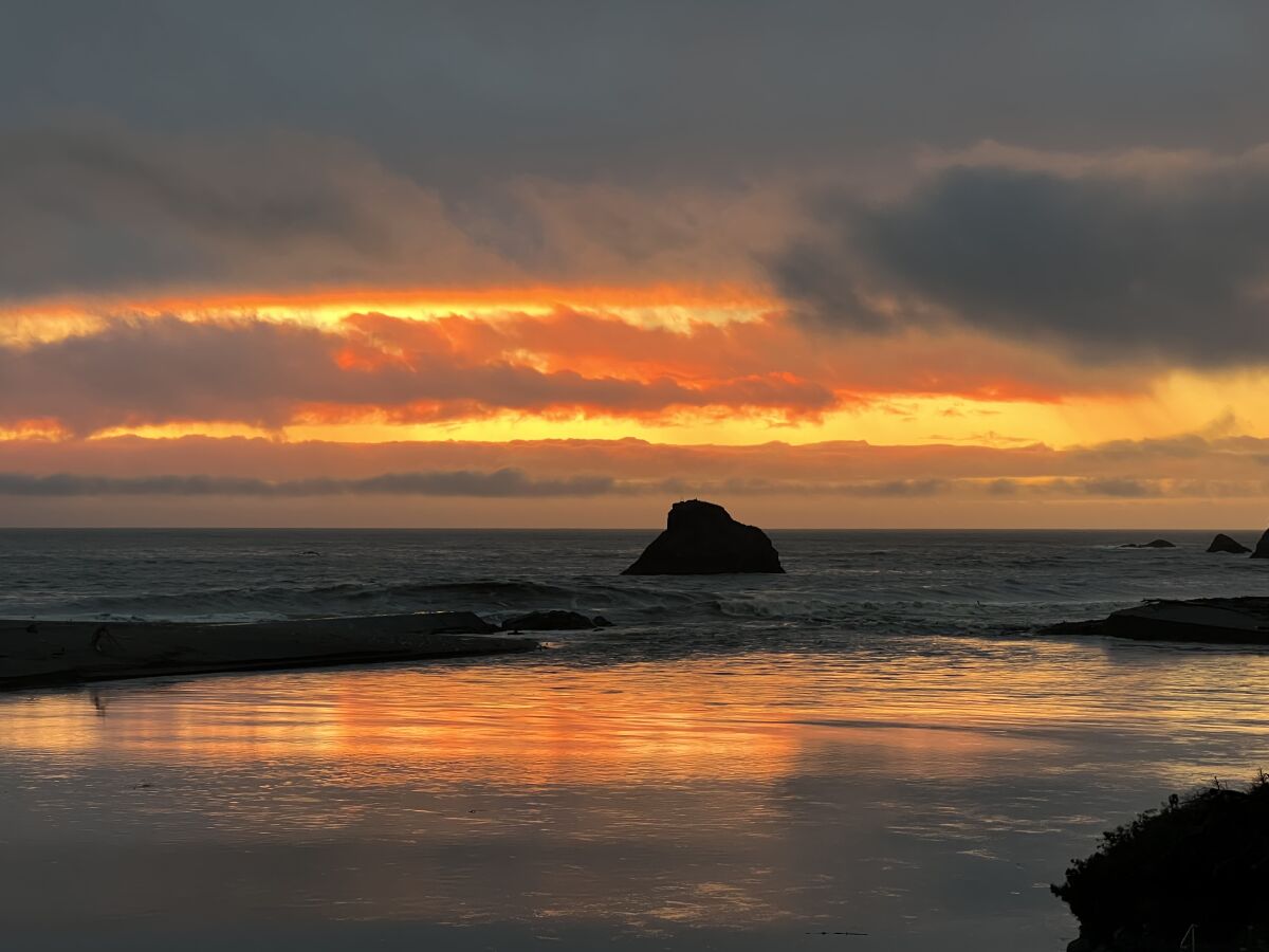 A large rocks jutting out of the ocean on a beach at sunset.