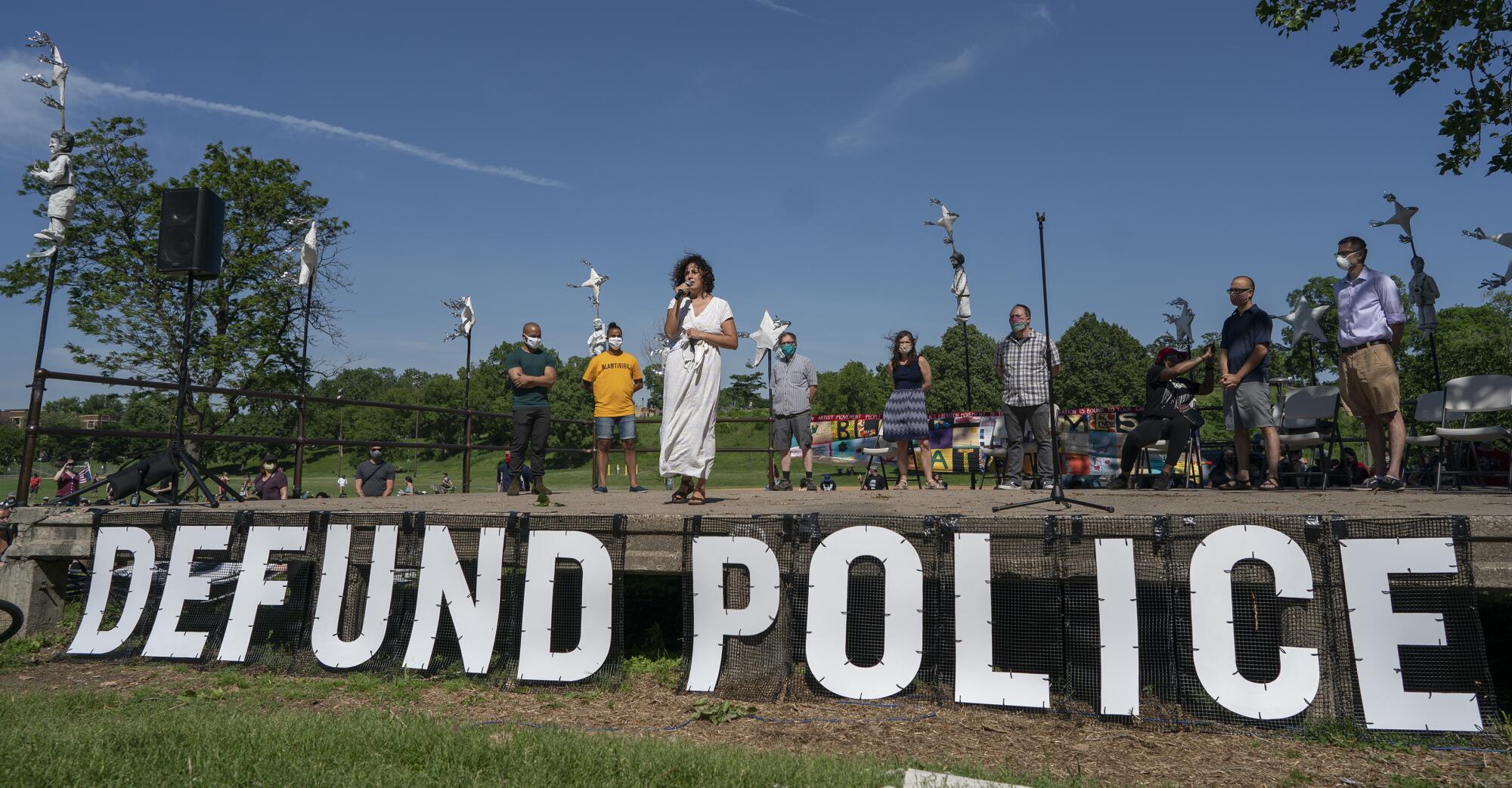 A speaker stands before a "Defund Police" sign