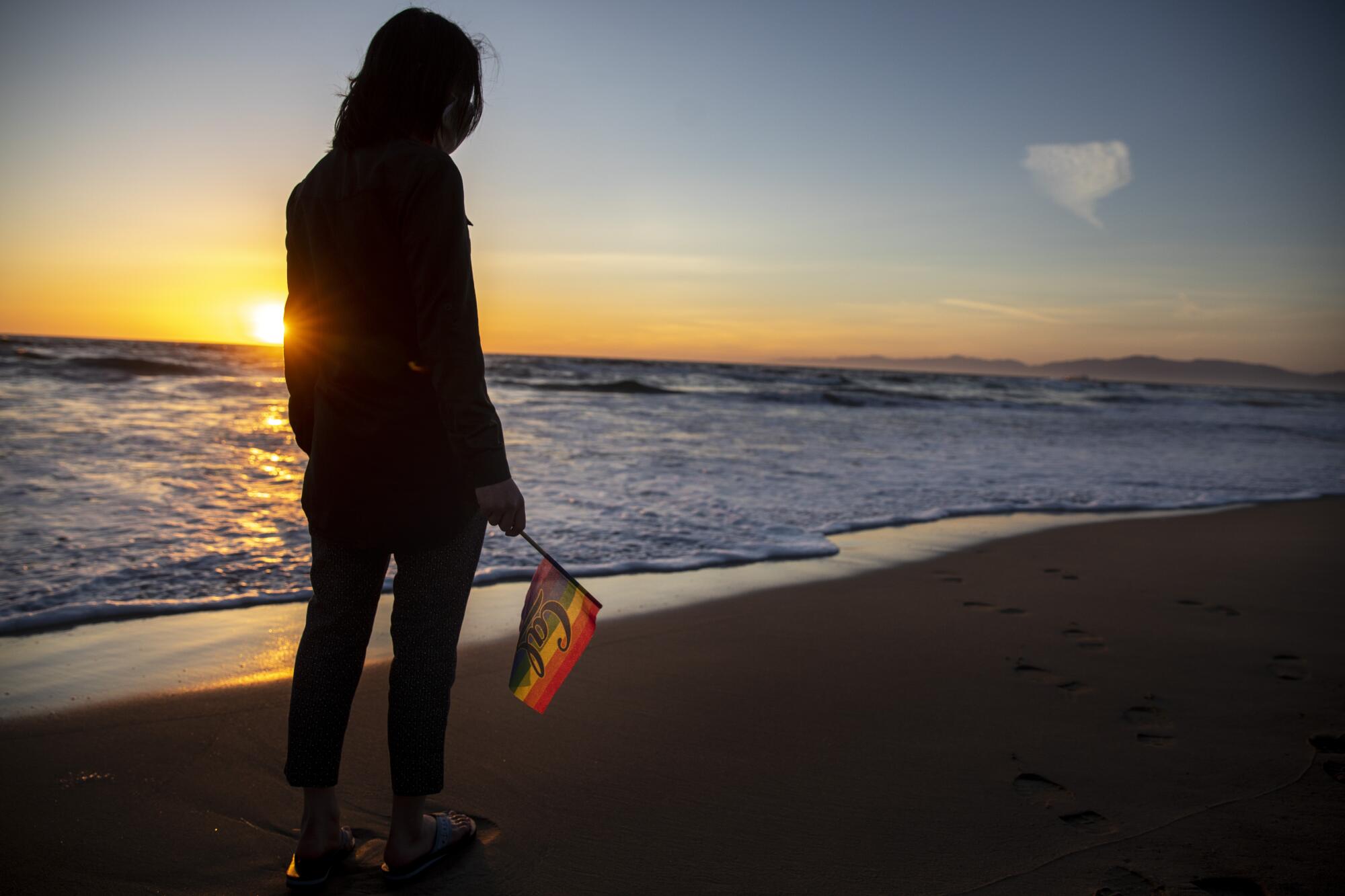 A person on the beach holding a pride flag.