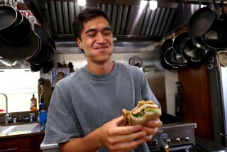 VENICE, CA - AUGUST 28, 2024 - Food content creator Owen Han, known as the "Sandwich King," enjoys a bite of his OG Spicy Chicken Sandwich in his studio, kitchen in Venice on August 28, 2024. Han is known for sharing creative sandwich recipes with his TikTok, YouTube and Instagram followers. Han started making videos in his apartment while attending USC. He has over 4 million followers. He is the author of the book, "Stacked - the art of the perfect sandwich." (Genaro Molina/Los Angeles Times)