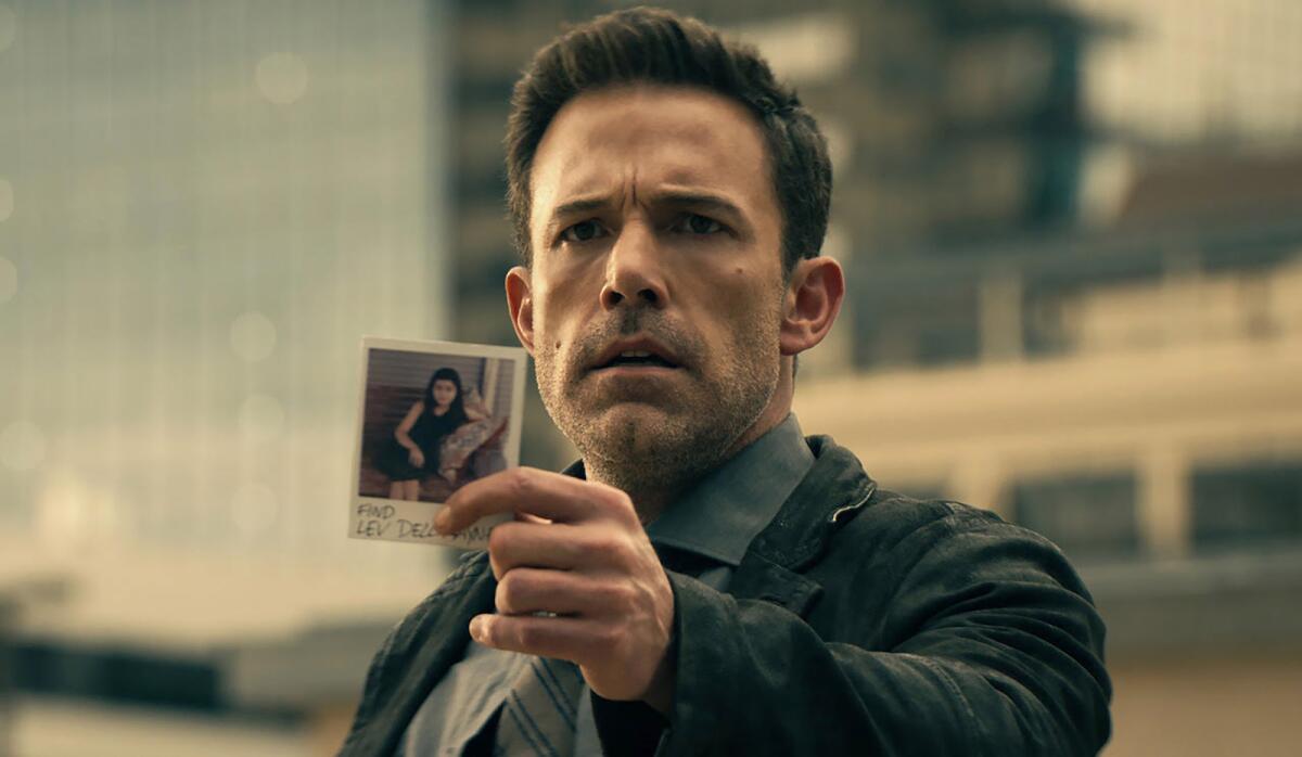 A serious-looking Ben Affleck holds up a Polaroid of a young girl.