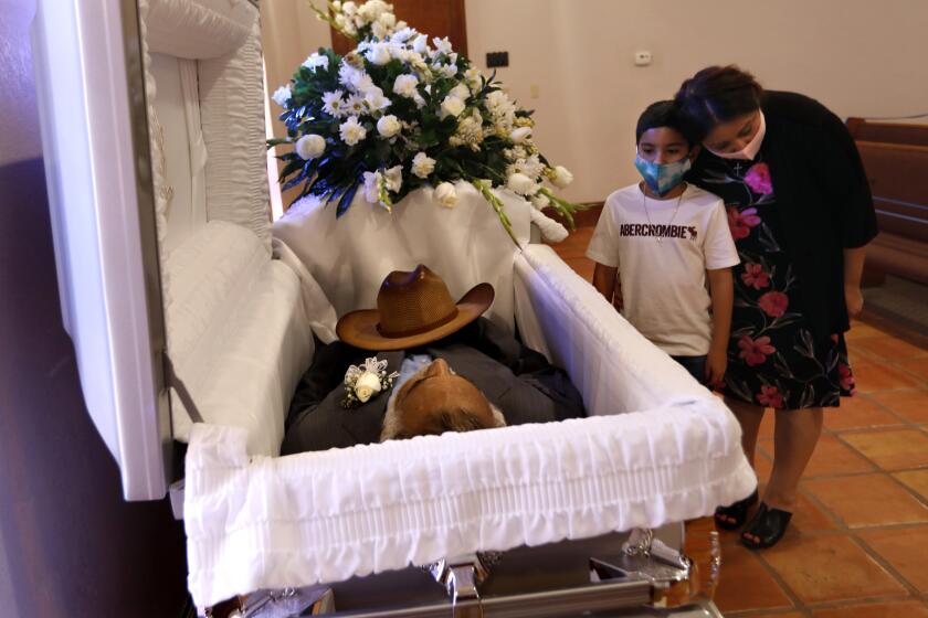 MC ALLEN, TEXAS-July 20, 2020-Sonia Aguirre, right, and 9-years-old Abdiel Sanchez pays respect to his great grandfather Fernando Aguirre, who passed away at age 69 from COVID-19. Fernando's wife is struggling for her life with coronavirus. The coronavirus is spreading rapidly through the Rio Grande Valley in Texas, where people of all ages are getting infecting at family gatherings. (Carolyn Cole/Los Angeles Times)