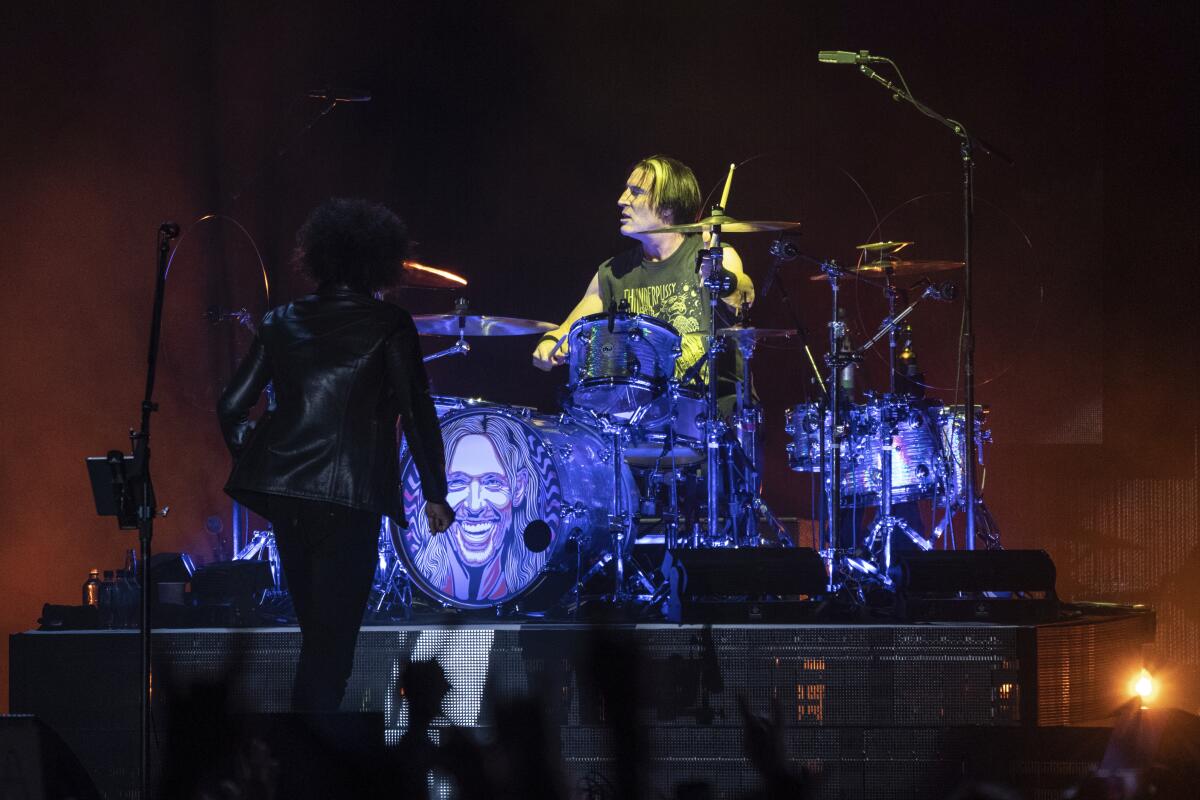 Sean Kinney playing a full drum kit on a raised platform on a stage