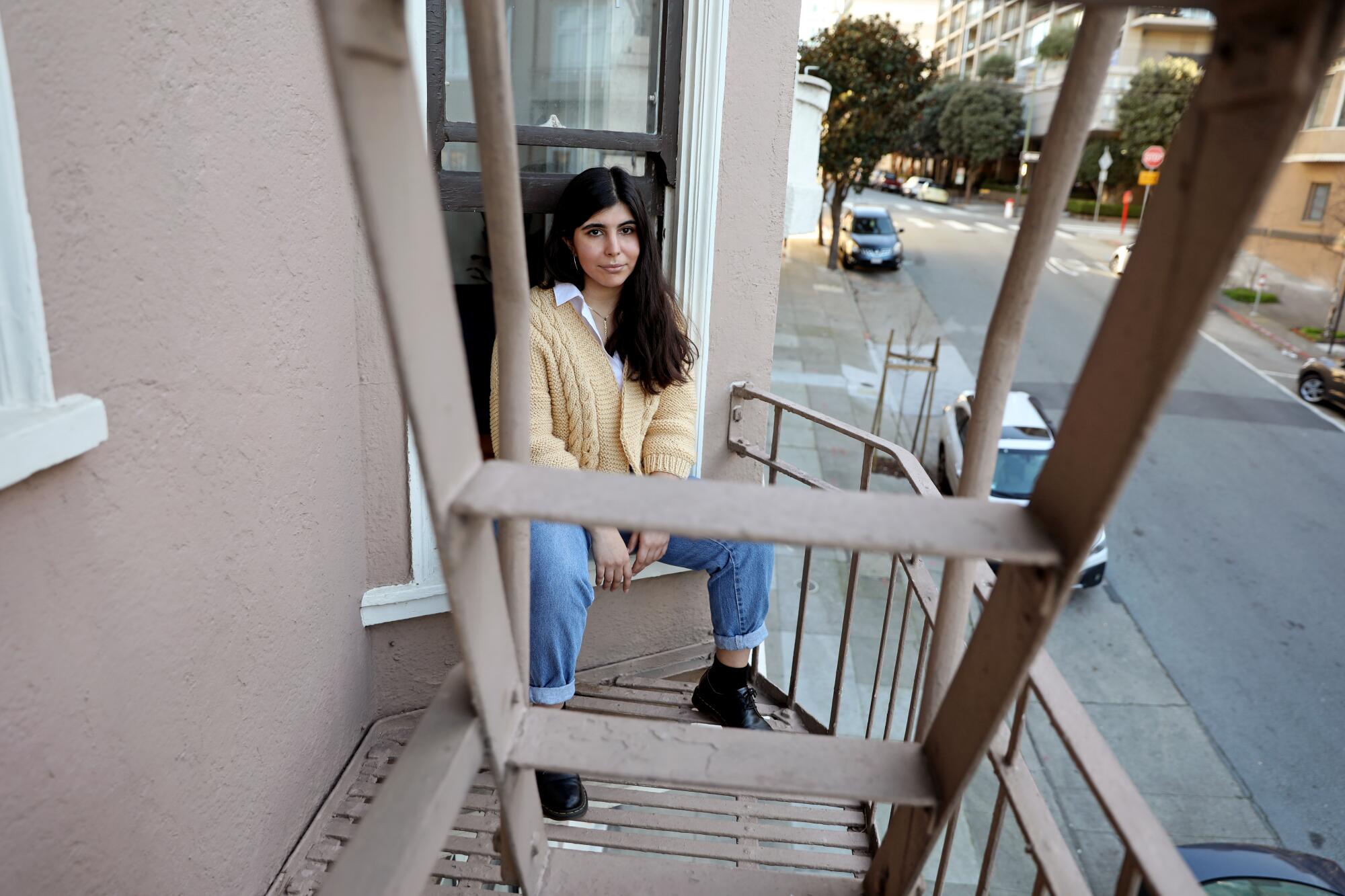 Sarah Abdeshahian sits on the window sill of her apartment.