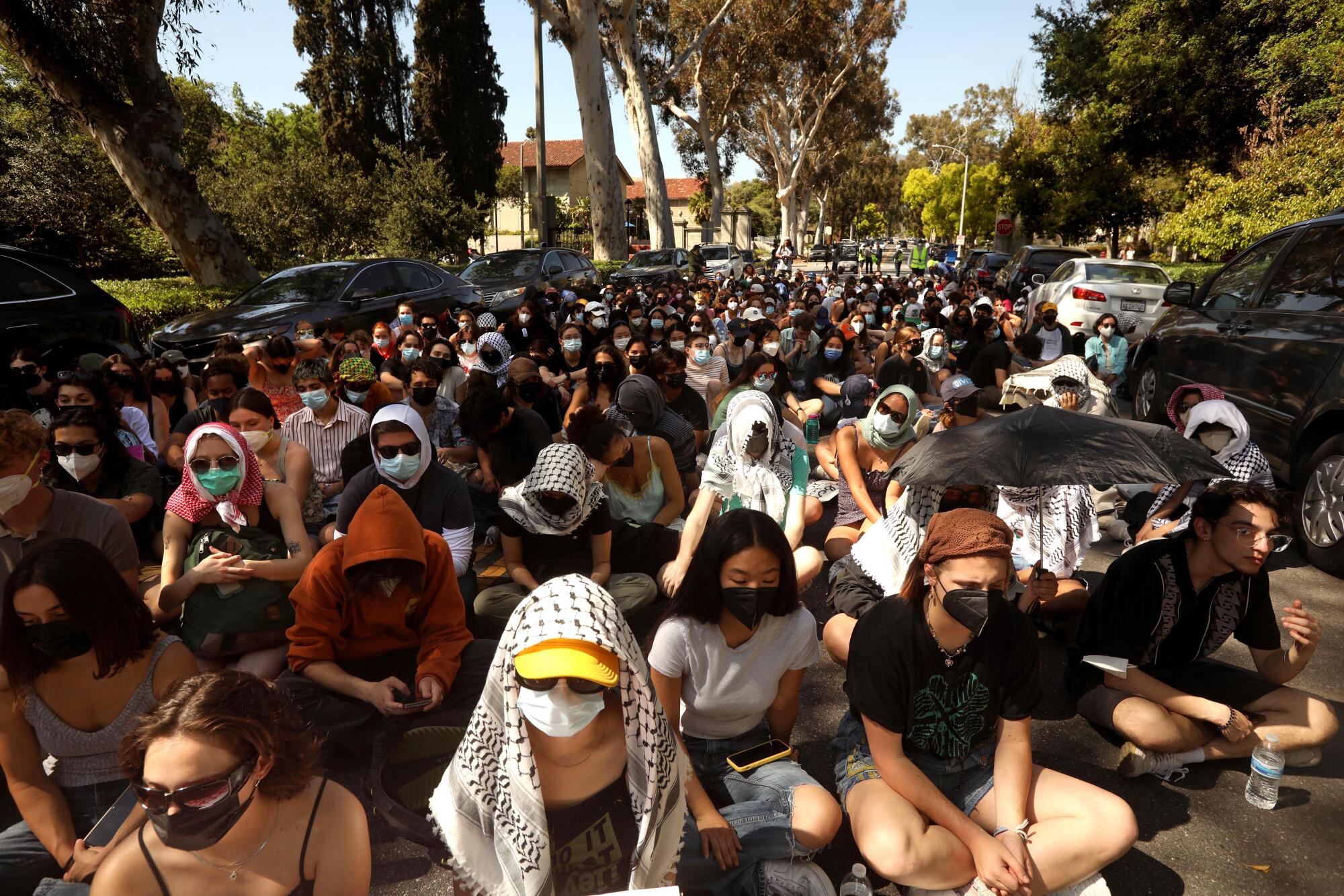 Hundreds of Pomona College students and others sit together on a section of street in front of a building.