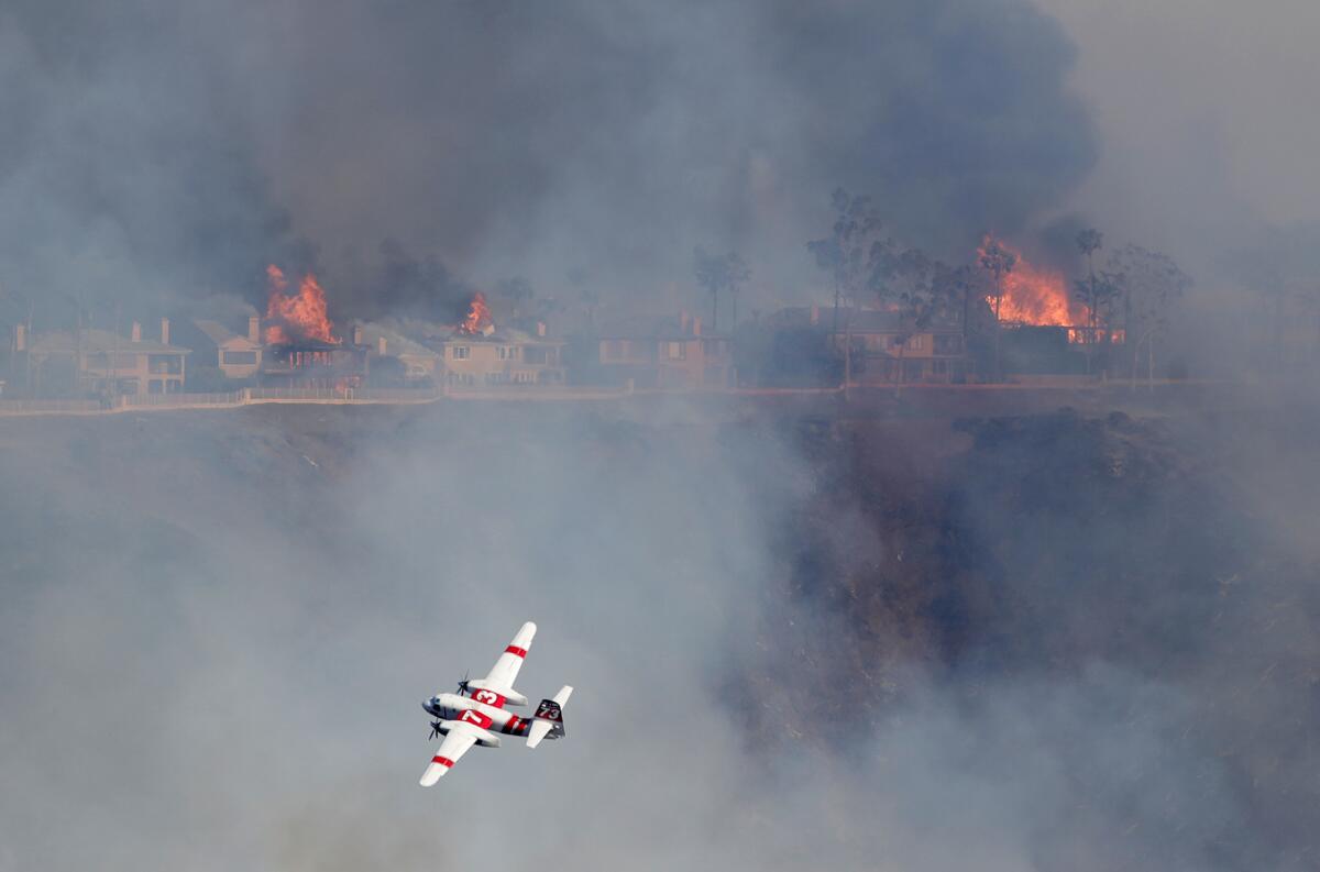 A Cal Fire firefighting air tanker drops fire retardant on a hillside as homes burn on Pacific Island Drive in Laguna Niguel.