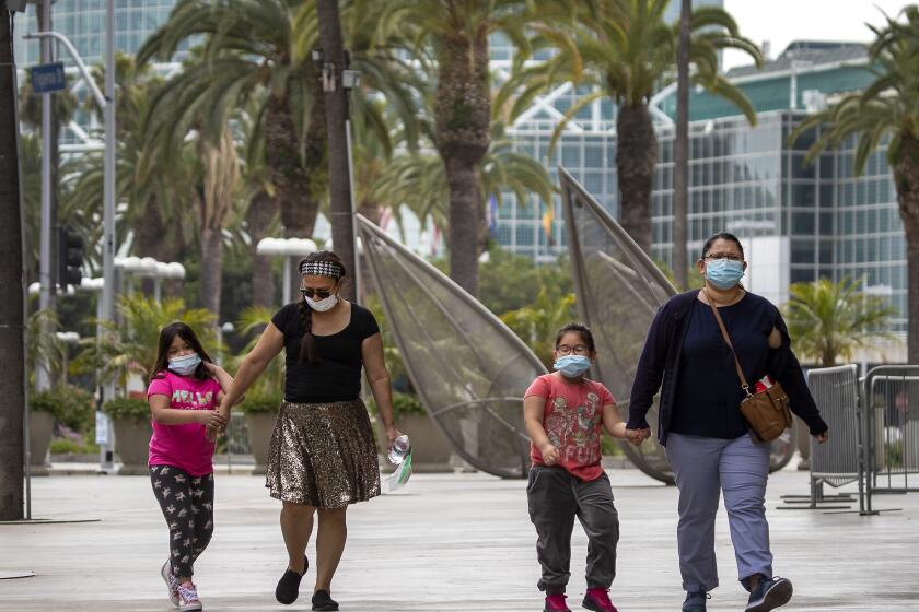 LOS ANGELES, CA - JUNE 18: From left: Ana Morales and granddaughter Hannah Paredes, 8, and Julie Rodriguez and niece Paige Paredes, 6, all of Los Angeles, walk to the grocery store and wear protective masks to protect from contracting COVID-19 while walking by the Staples Center Thursday, June 18, 2020 in Los Angeles, CA. Gov. Gavin Newsom on Thursday ordered all Californians to wear face coverings while in public or high-risk settings, including when shopping, taking public transit or seeking medical care, following growing concerns that an increase in coronavirus cases has been caused by residents failing to voluntarily take that precaution. (Allen J. Schaben / Los Angeles Times)