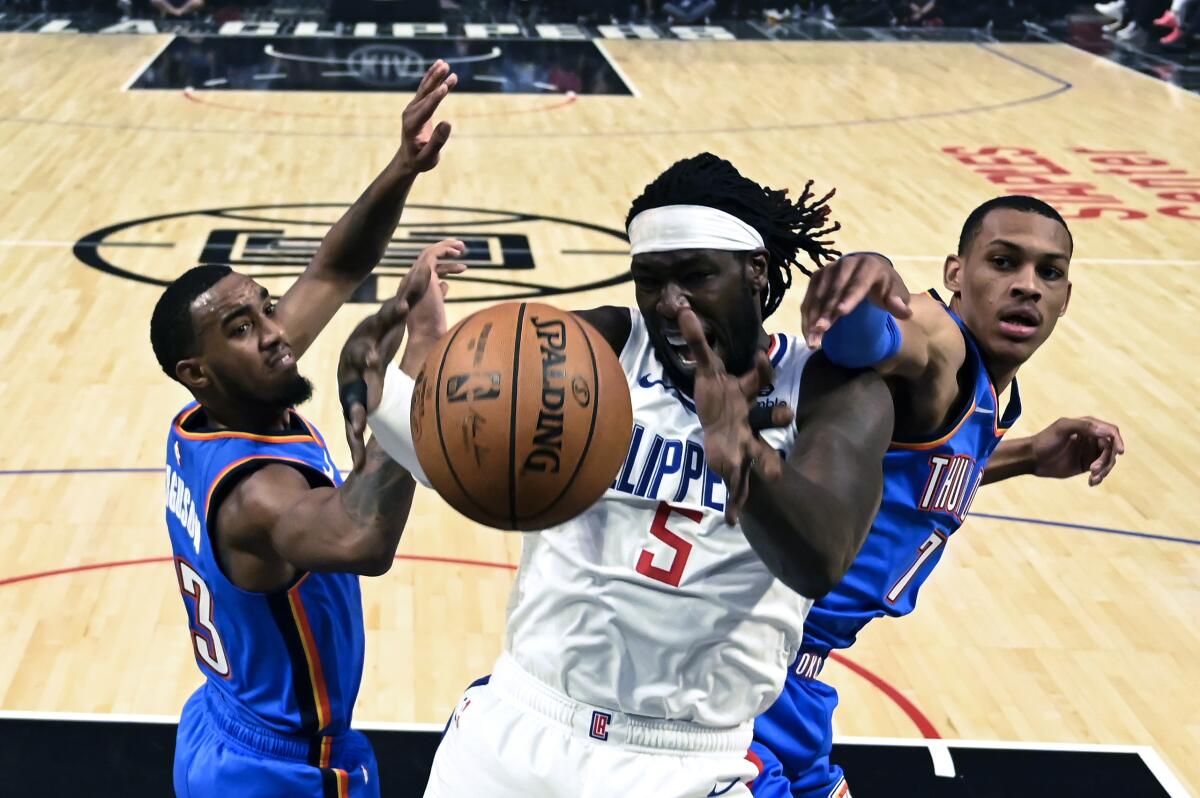 Clippers forward Montrezl Harrell (5) fights for a rebound with Thunder guard Terrance Ferguson (23) and forward Darius Bazley (7) during a game Nov. 18 at Staples Center.