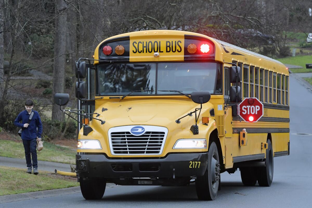 FILE -A Cobb County School bus moves on street Friday, March 13, 2020, in Kennesaw, Ga. Georgia's second-largest school district on Thursday, July 14, 2022 approved a policy allowing some employees who aren't certified police officers carry guns in schools, but excluded teachers from those who can be armed. (AP Photo/Mike Stewart, File)