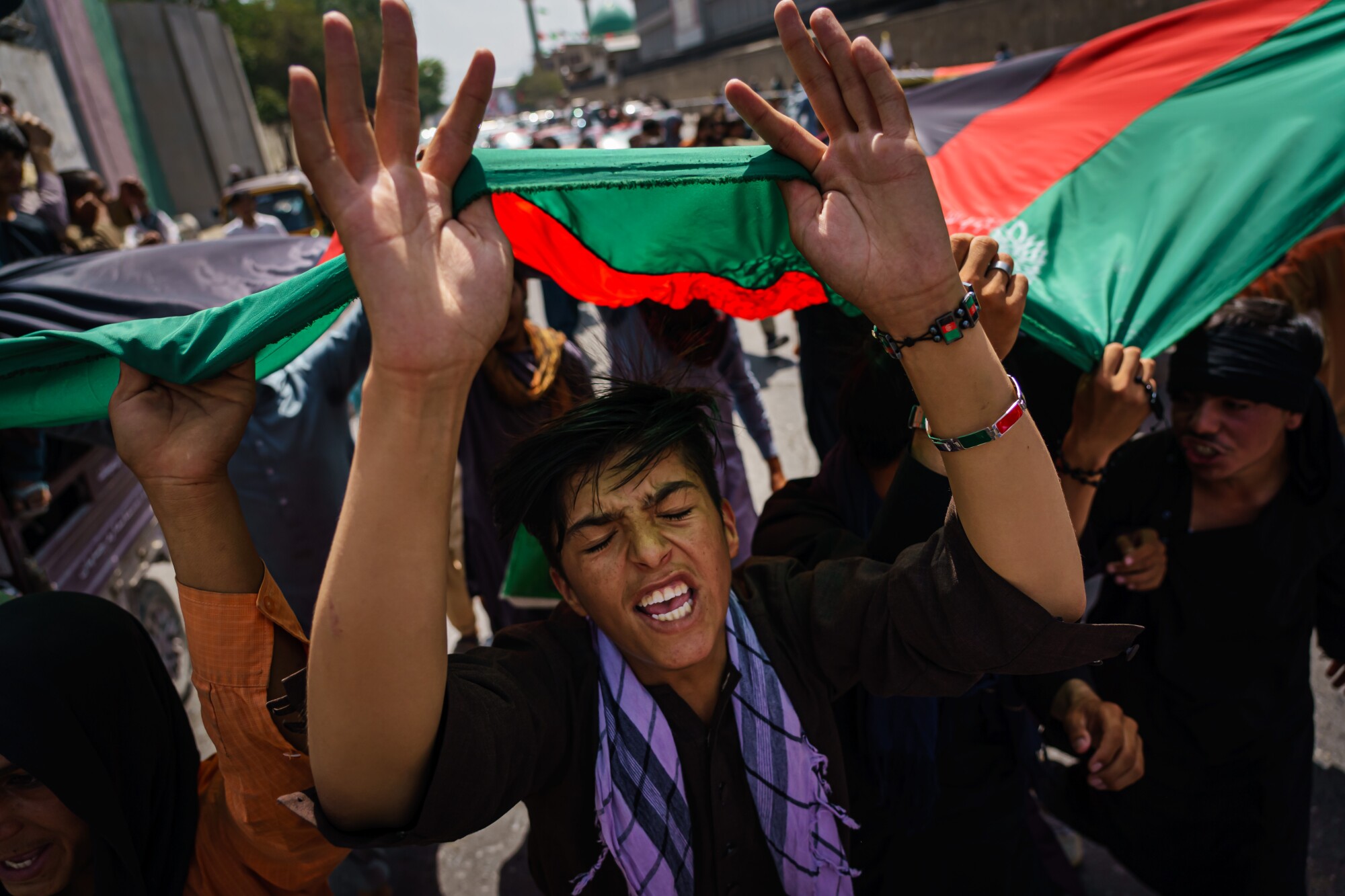 Afghans march down the street carrying  the national flag