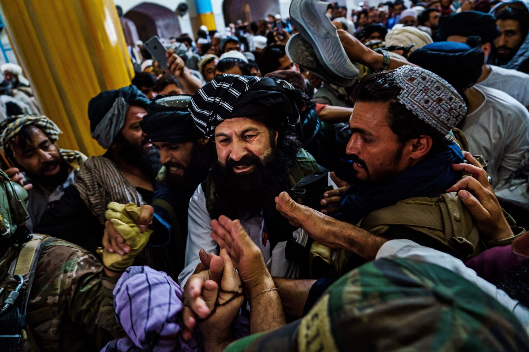 Hands reach out from a swarm of people surrounding a bearded smiling man moving through the crowd.