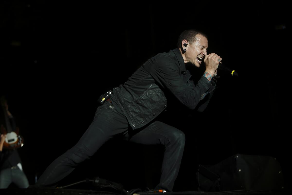 Chester Bennington of Linkin Park wearing all black and lunging while singing onstage