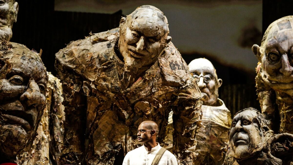 Sean Panikkar as Gandhi surrounded by puppets of hostile bigwigs incensed by his nonviolent activism in South Africa in Los Angeles Opera's production of "Satyagraha" by Philip Glass.