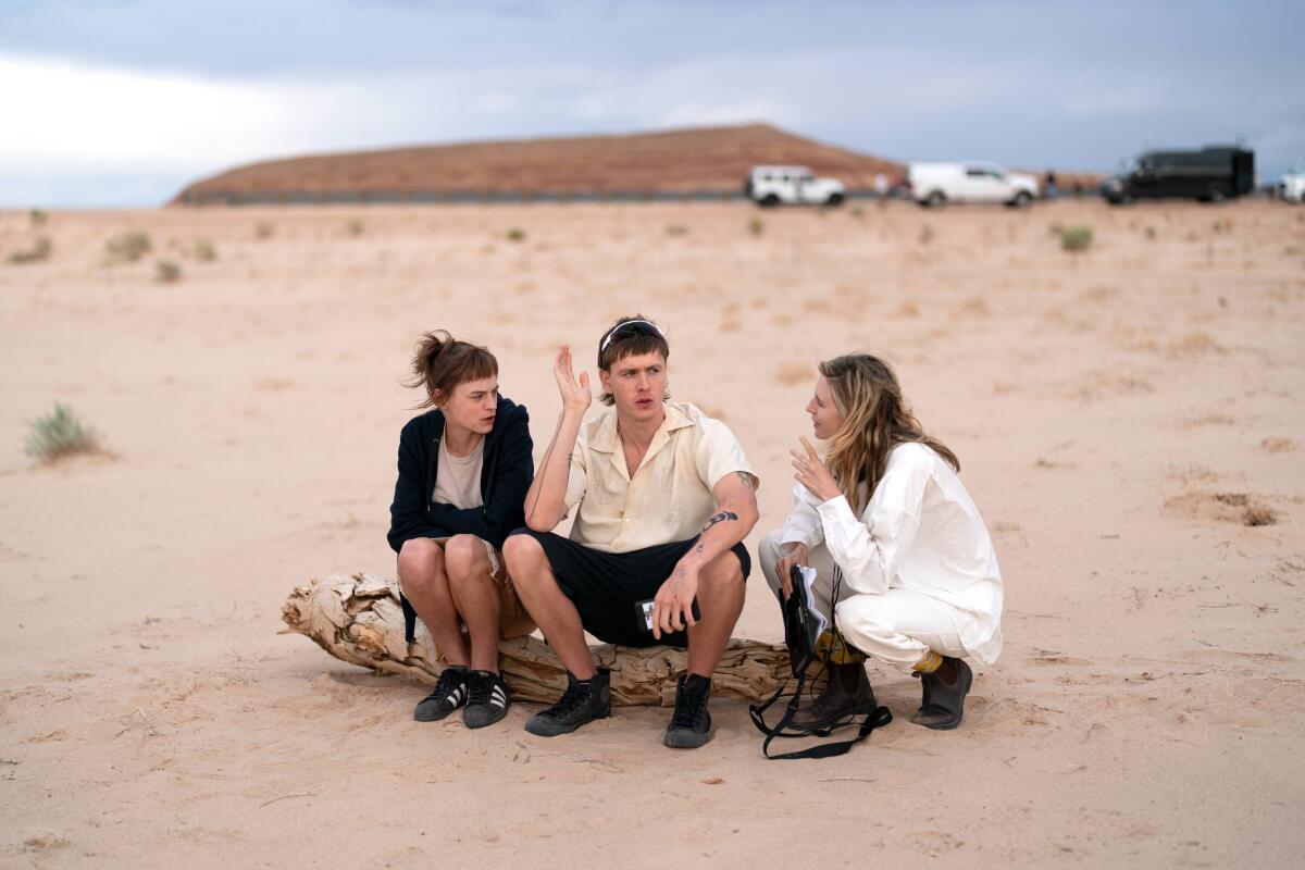 Two actors sit on a log in the desert, having a discussion with their director.
