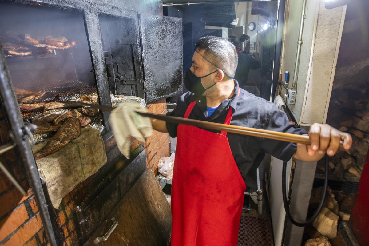 A pitmaster inspects meat in a smoker.