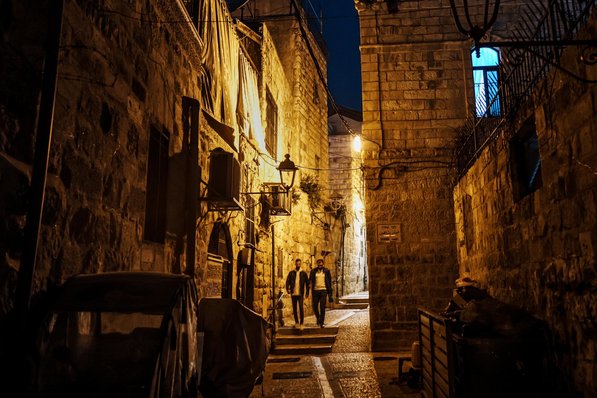 Two people walk through an alleyway.