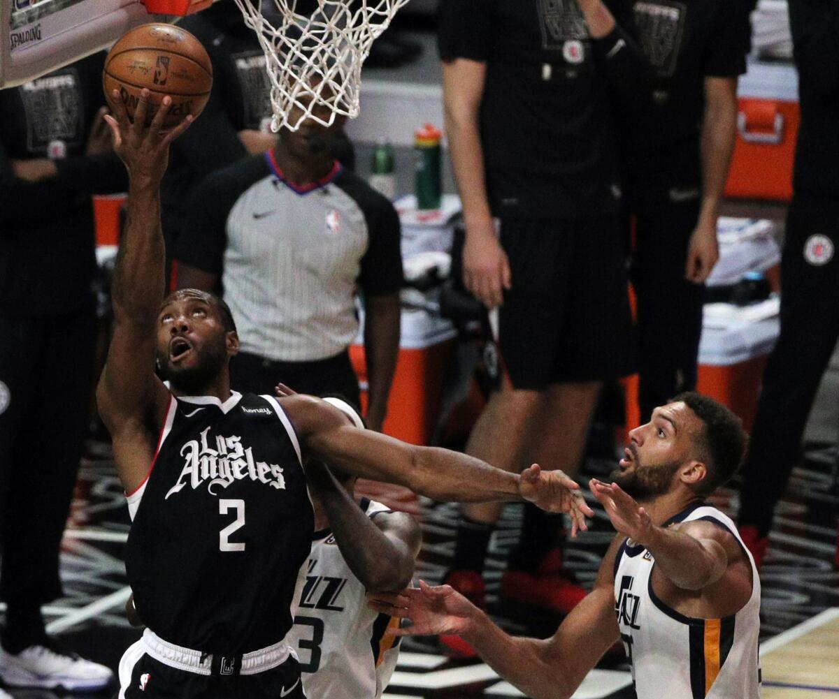 The Clippers' Kawhi Leonard scores on a reverse layup against the Jazz's Royce O'Neale, rear, and center Rudy Gobert, right.
