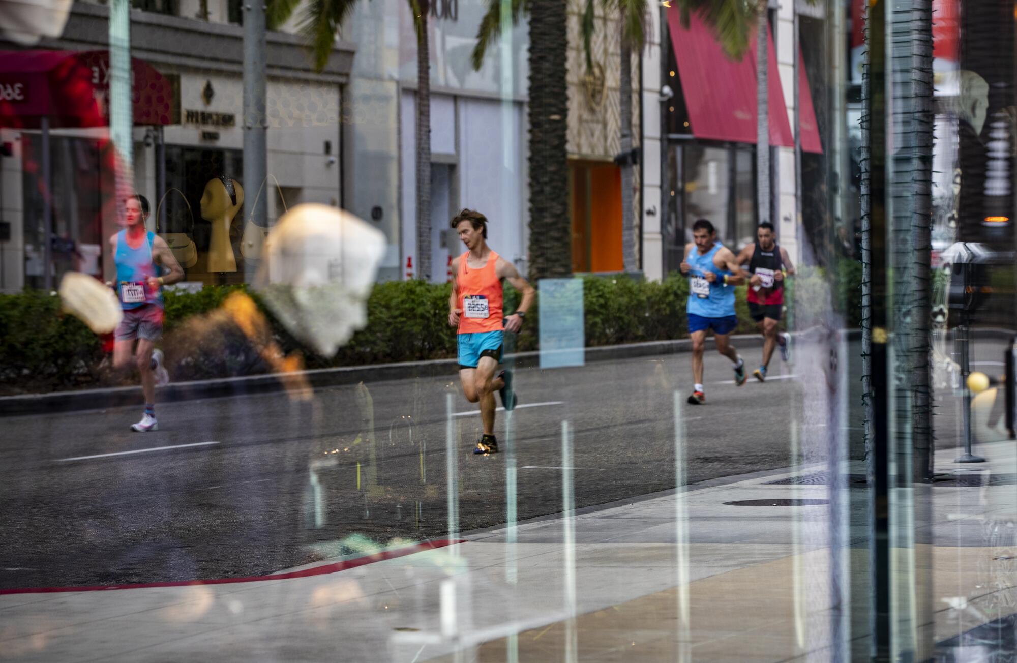 Runners are reflected in the front window of the Prada store on Rodeo Drive