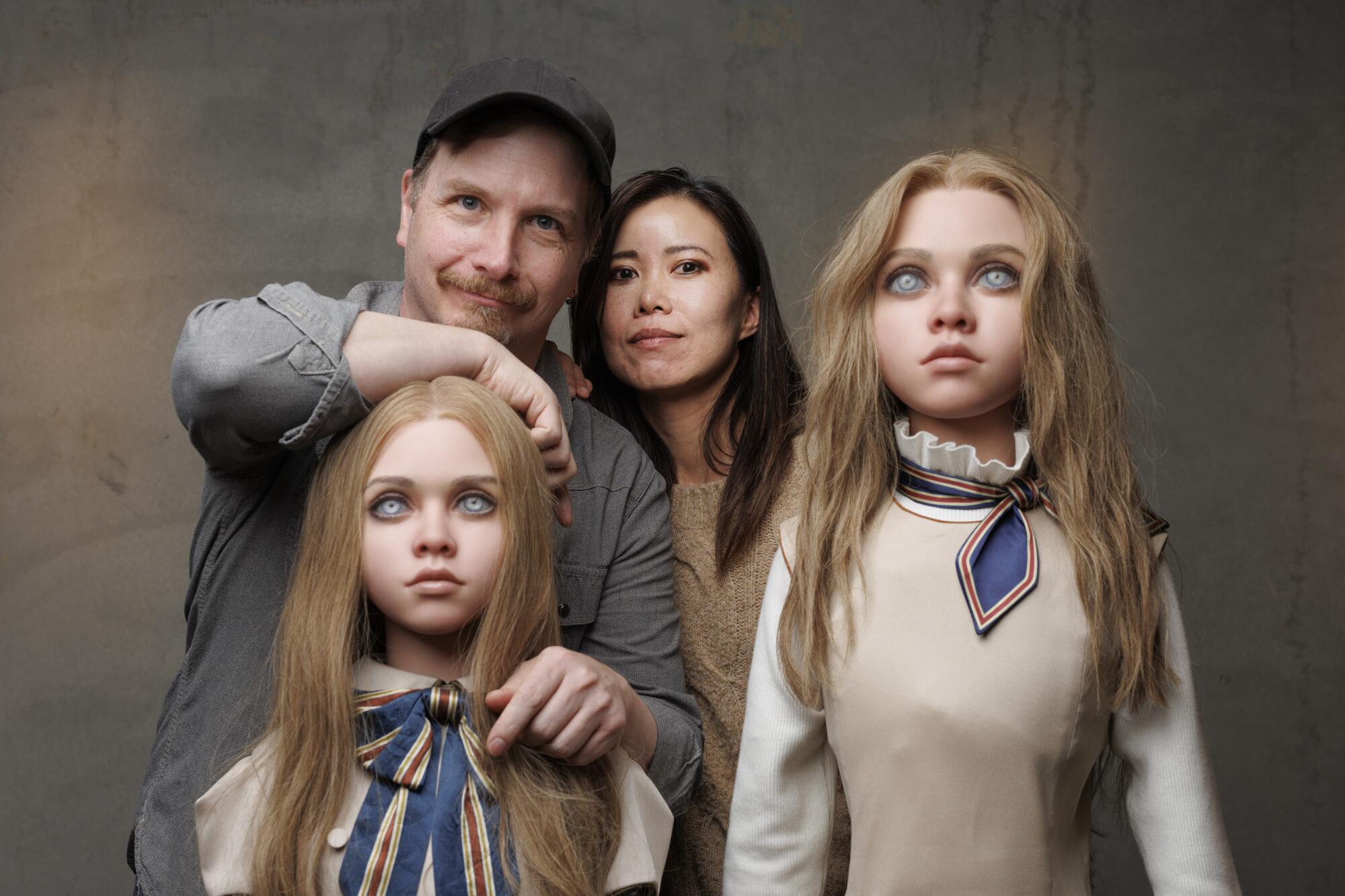A smiling man and woman pose with two murderous-looking horror dolls.