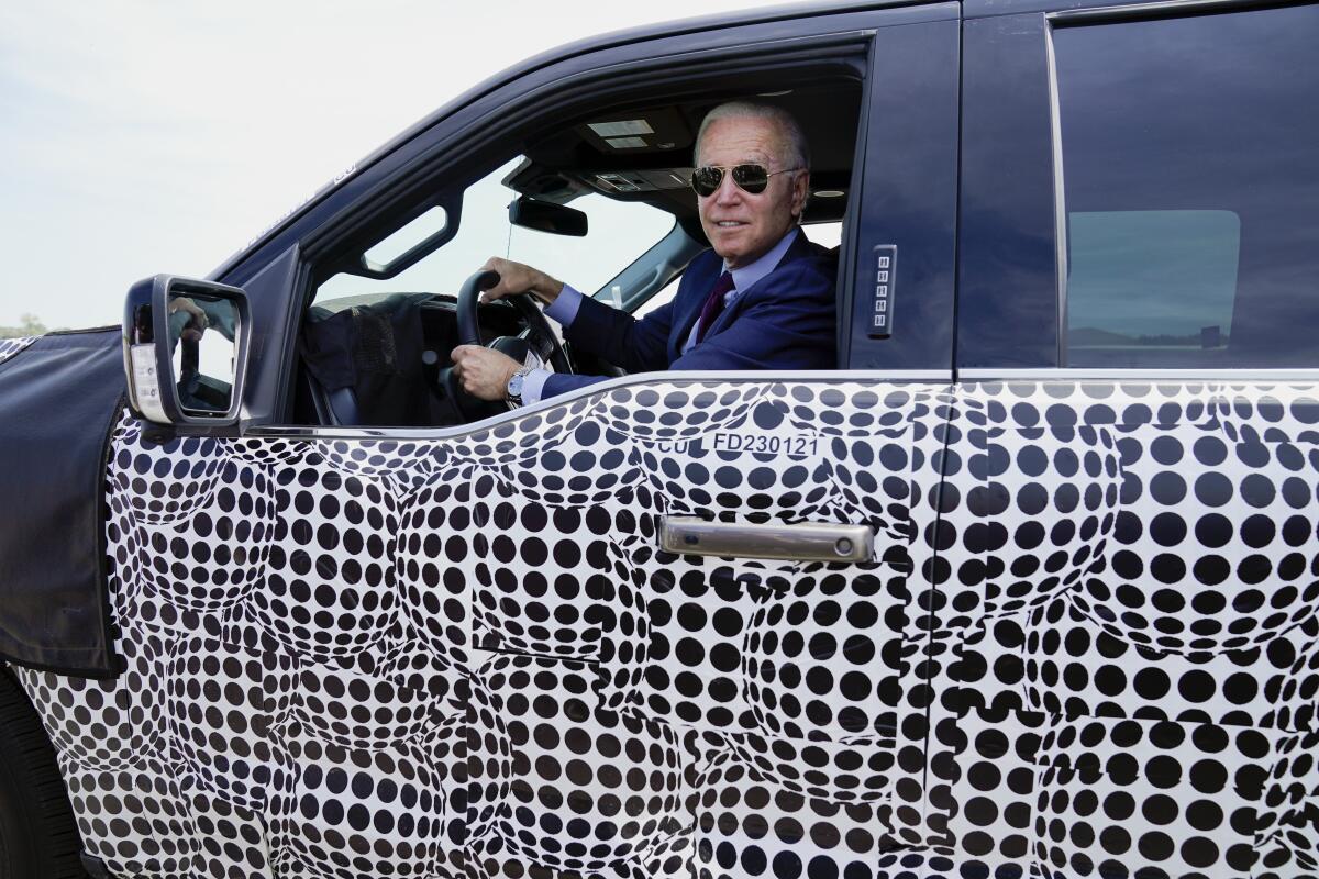 President Joe Biden stops to talk to the media as he drives a Ford F-150 Lightning truck 