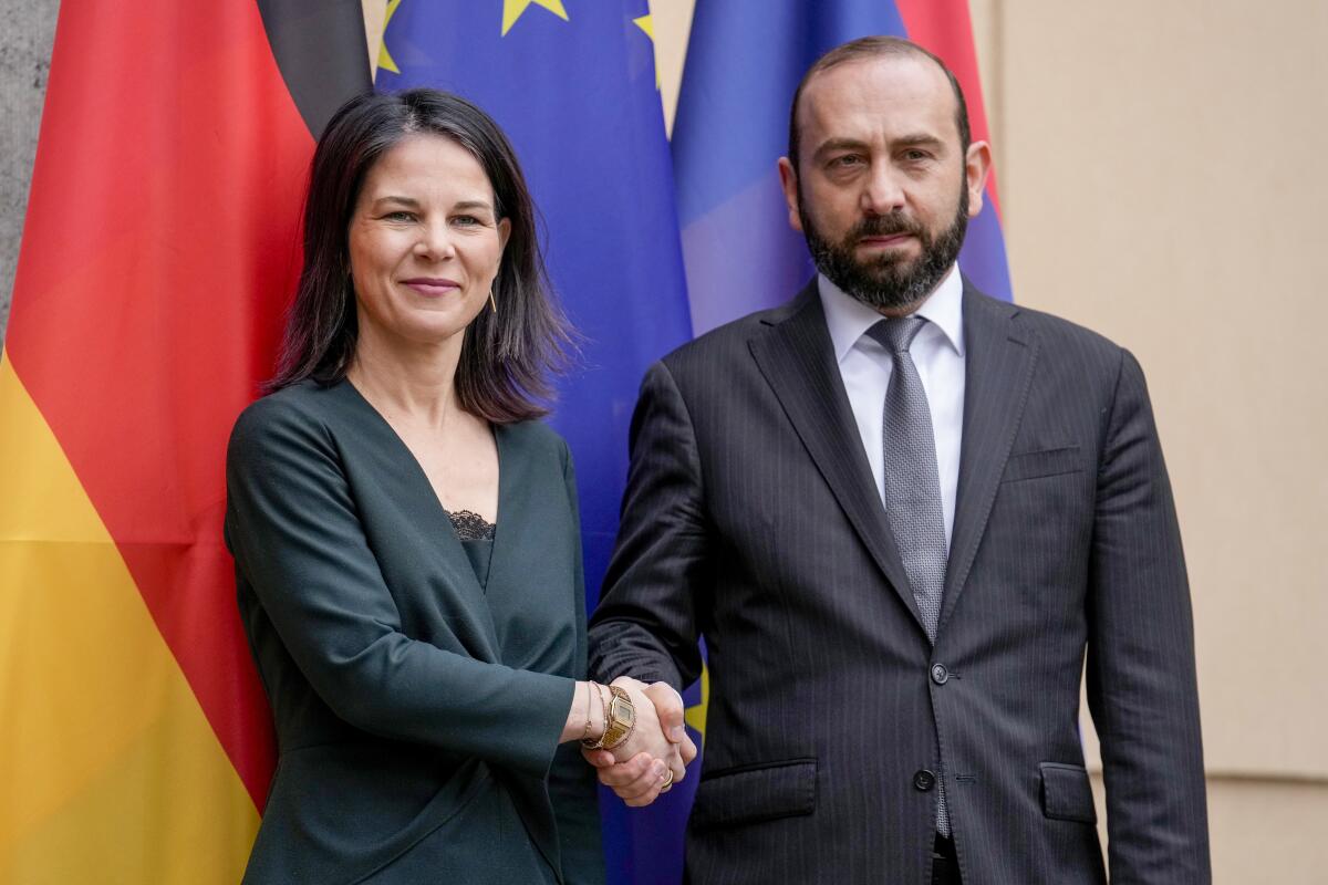 Annalena Baerbock and Ararat Mirzoyan shake hands, with flags behind them