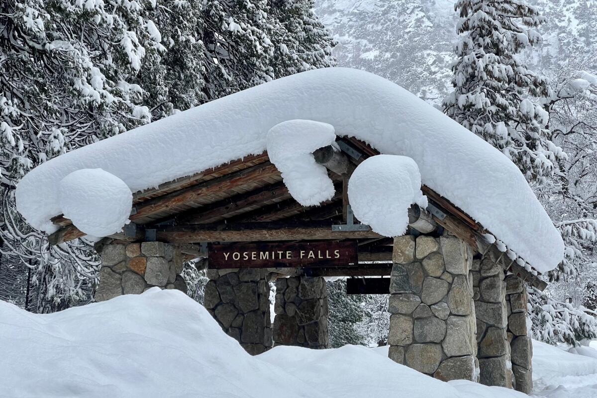 Snow covers the roof of an outdoor structure with the words "Yosemite Falls" on it.