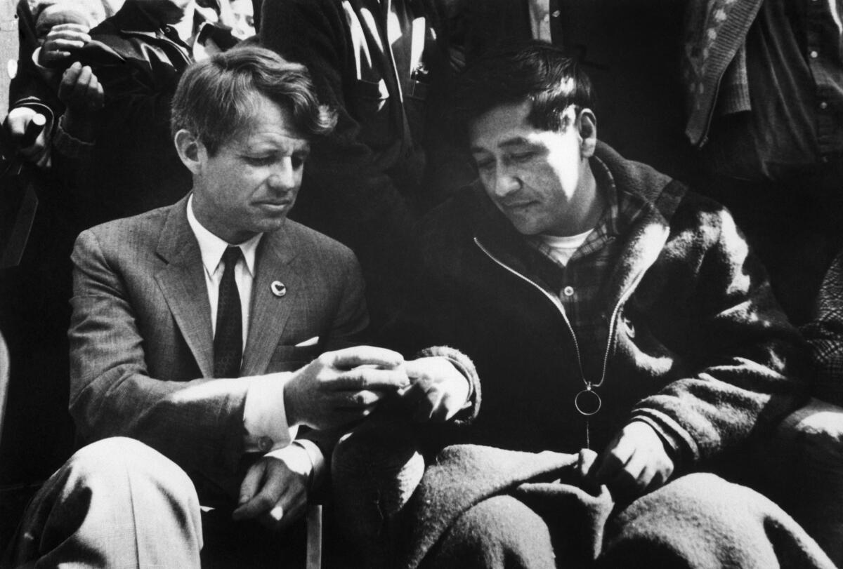 A black-and-white photo of Robert F. Kennedy and Cesar Chavez sitting and breaking bread