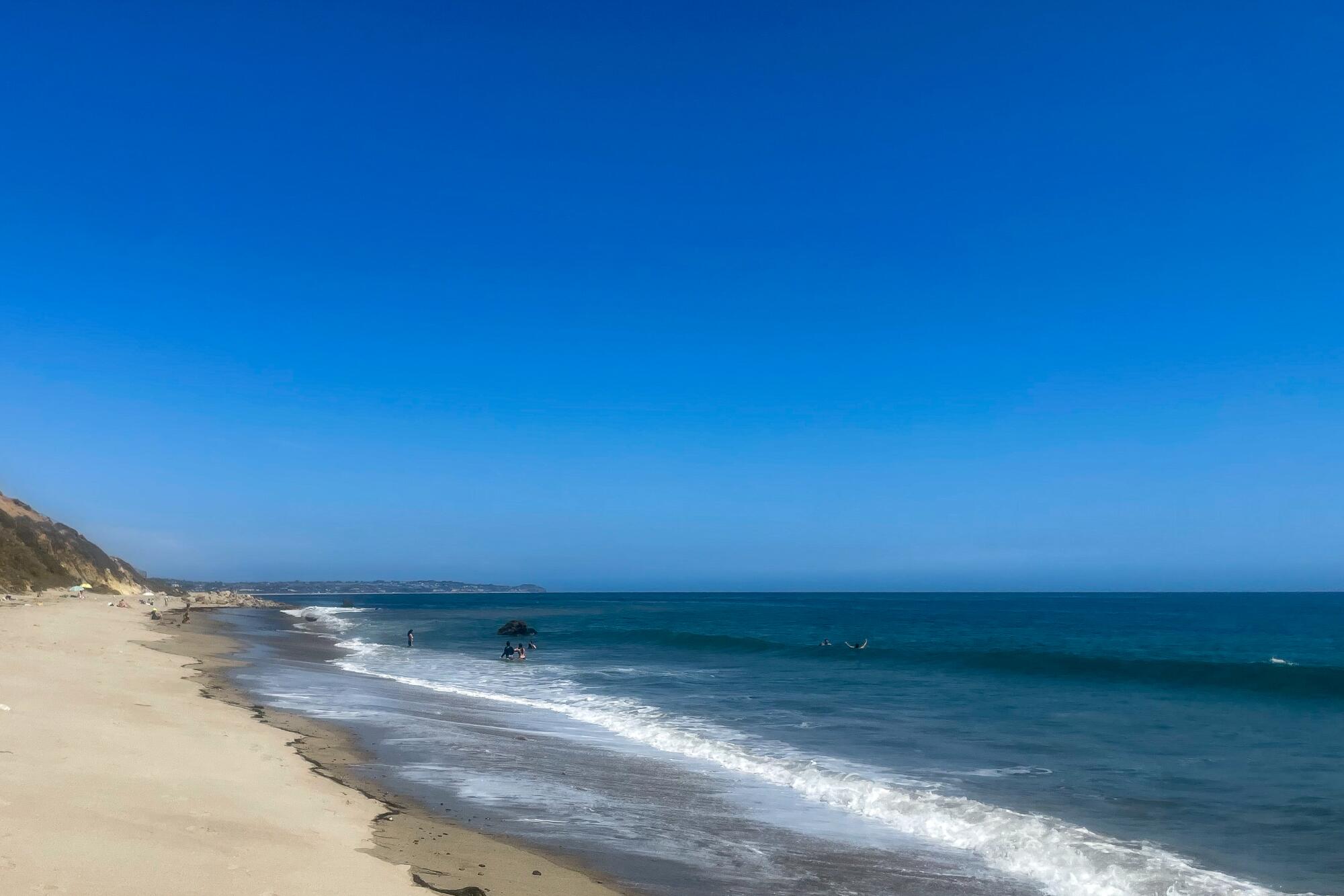 White foamy waves kiss the sand with a blue sky above.