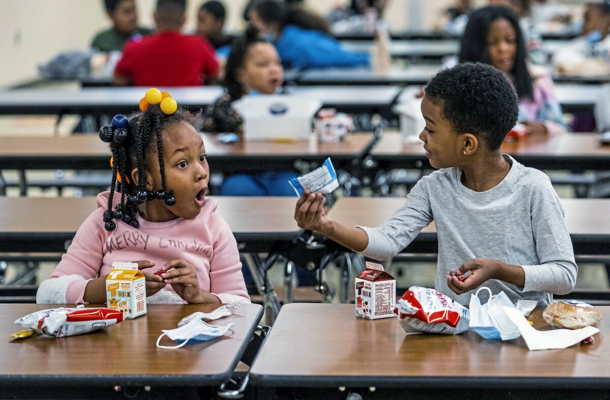 Two kids show off their lunches at a school cafeteria table
