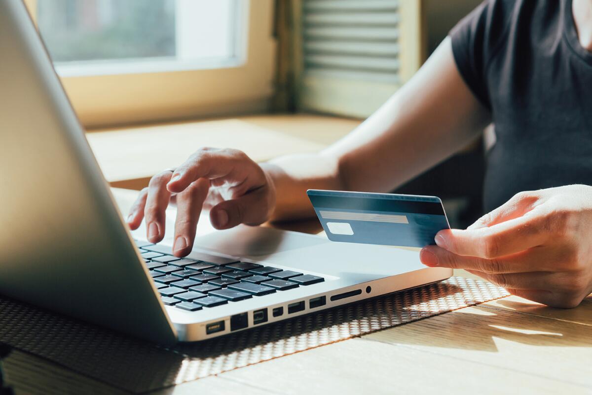 Online shopper entering personal information on a laptop while holding credit card