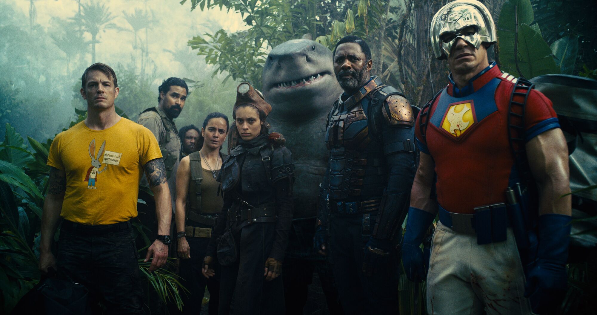 Seven people in combat gear and an anthropomorphic shark standing in a jungle