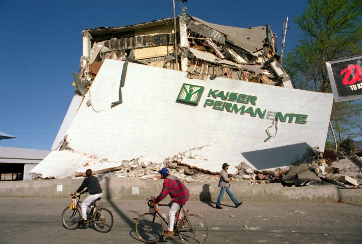 Cyclists roll past the remains of a Kaiser Permanente clinic and office building in Granada Hills that collapsed during the Northridge earthquake of 1994.
