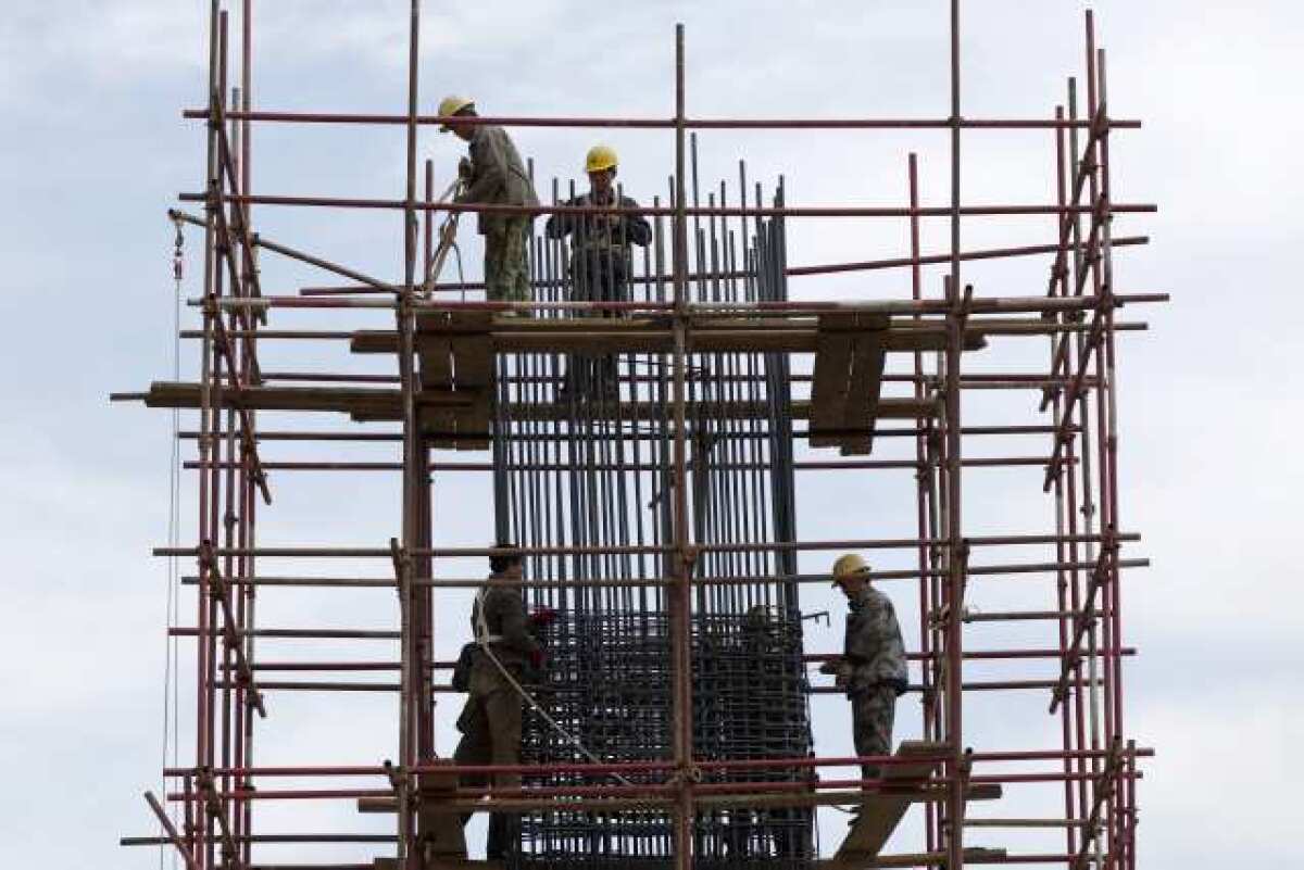 Workers stand on scaffolding at a road construction site in Beijing. Economic growth around the world, including in China, will continue, according to the IMF. But the environment remains fragile.