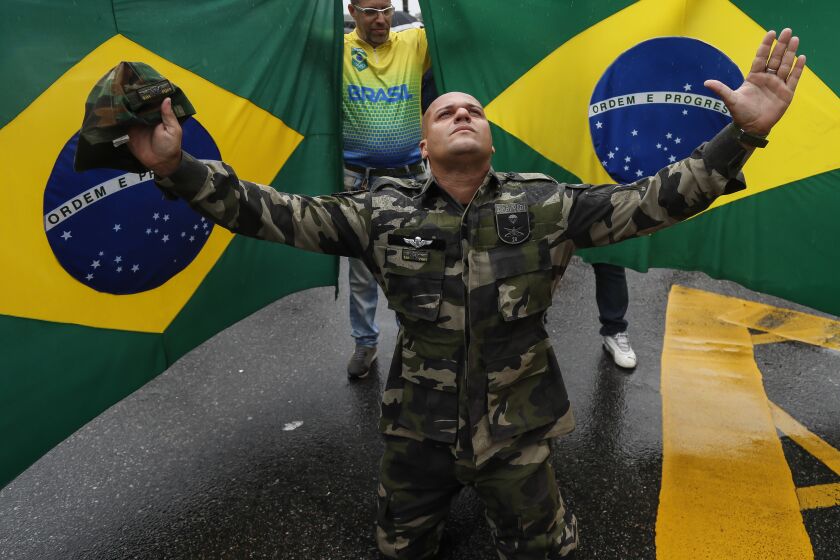 A supporter of President Jair Bolsonaro dressed in fatigues, kneels with his arms spread out in front of Brazilian national flags, during a protest against his defeat in the presidential runoff election, in Rio de Janeiro, Brazil, Wednesday, Nov. 2, 2022. Thousands of supporters called on the military Wednesday to keep the far-right leader in power, even as his administration signaled a willingness to hand over the reins to his rival Luiz Inacio Lula da Silva. (AP Photo/Bruna Prado)