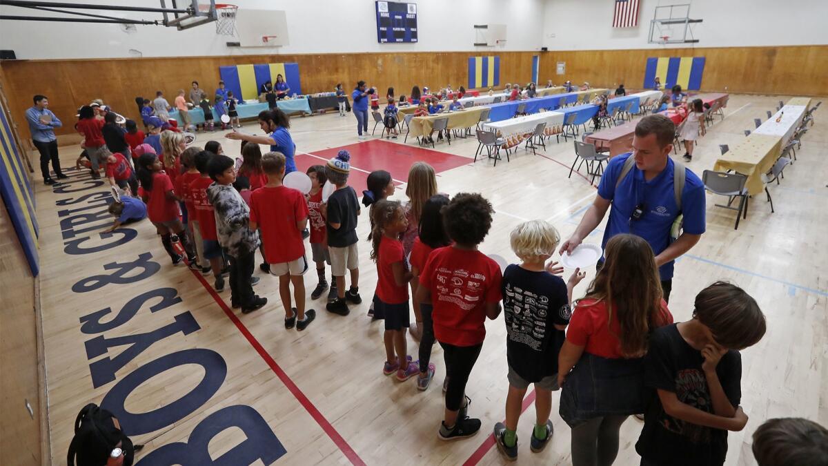 Instructors hand out paper plates as children line up for lunch in the gym at the Boys & Girls Club of Costa Mesa. The gym is scheduled to get new basketball hoops, rafters and paint in an upcoming renovation.