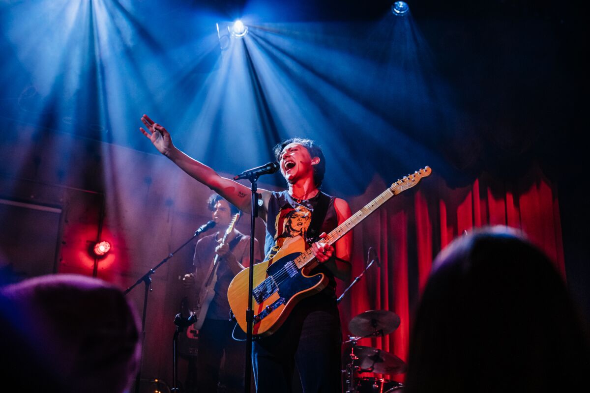Two actors portraying musicians onstage under colored lights.