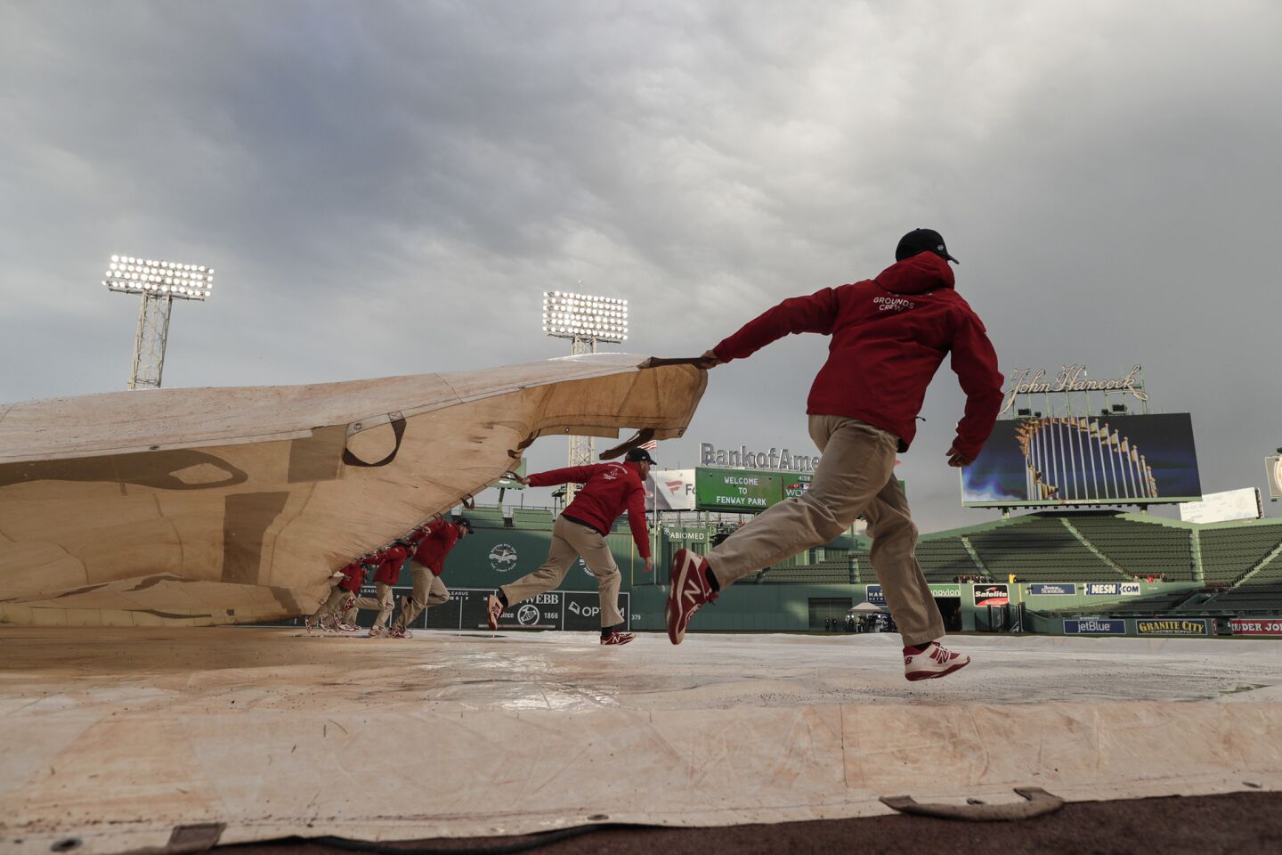 Ground crew members pull a tarp off the field soon after a heavy rainstorm passed by hours before the LA Dodgers and the Boston Red Sox play game one of the 2018 Word Series at Fenway Park.