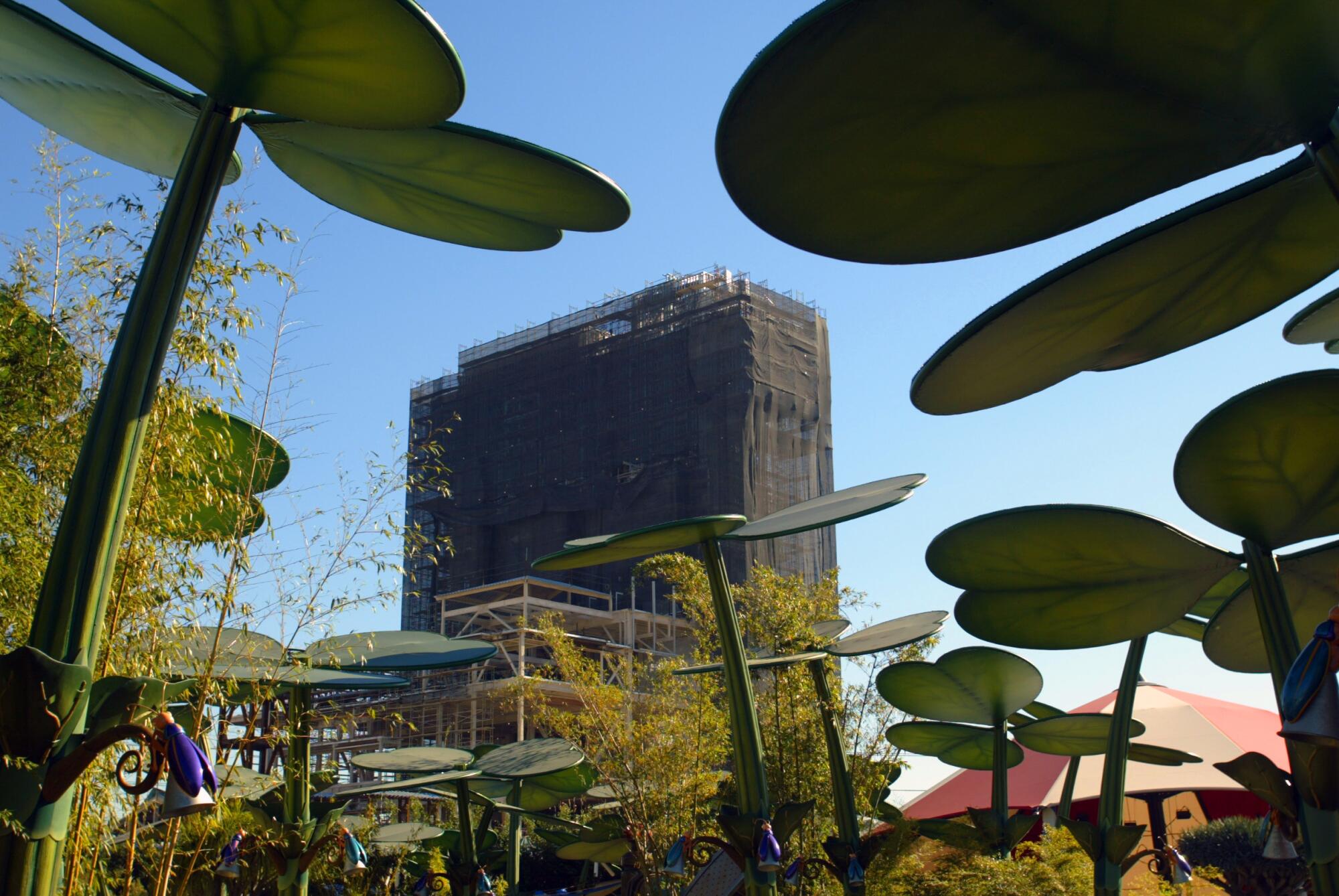 A photo of a tall structure wrapped in construction mesh, seen through giant plants.