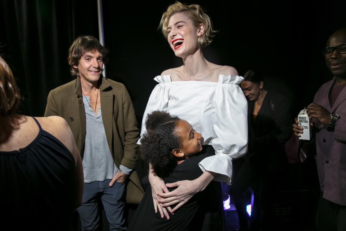 Elizabeth Debicki gets a hug from costar Viola Davis' daughter, Genesis. In the background are actor Lukas Haas, left, and director Steve McQueen, far right, backstage before a screening of their film "Widows" during the 2018 AFI Fest.