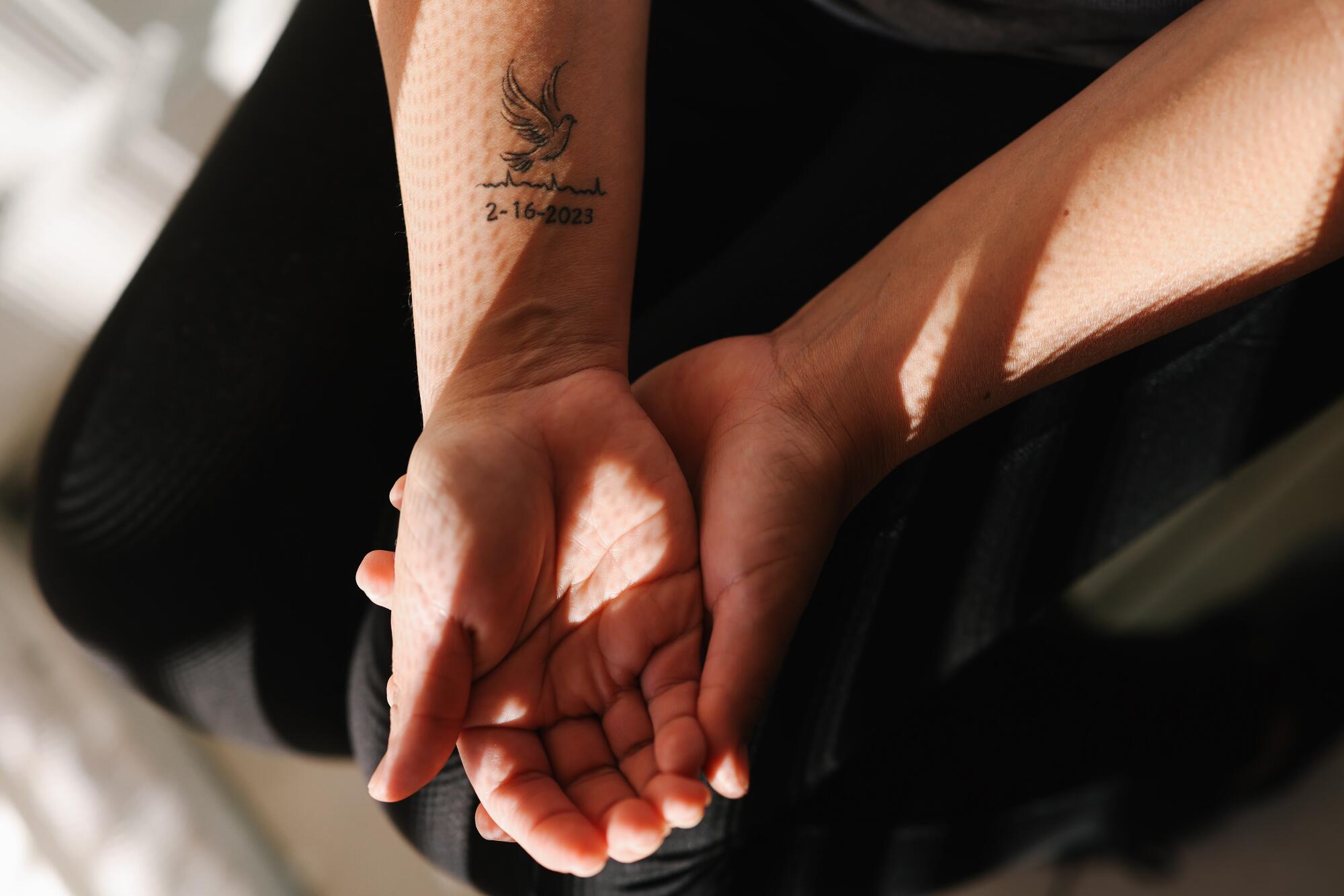 A woman shows a tattoo on the inside of her forearm.