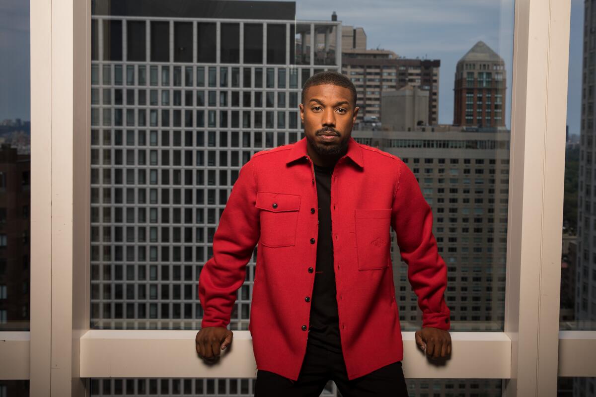 Michael B. Jordan, wearing a red top, stands for a portrait