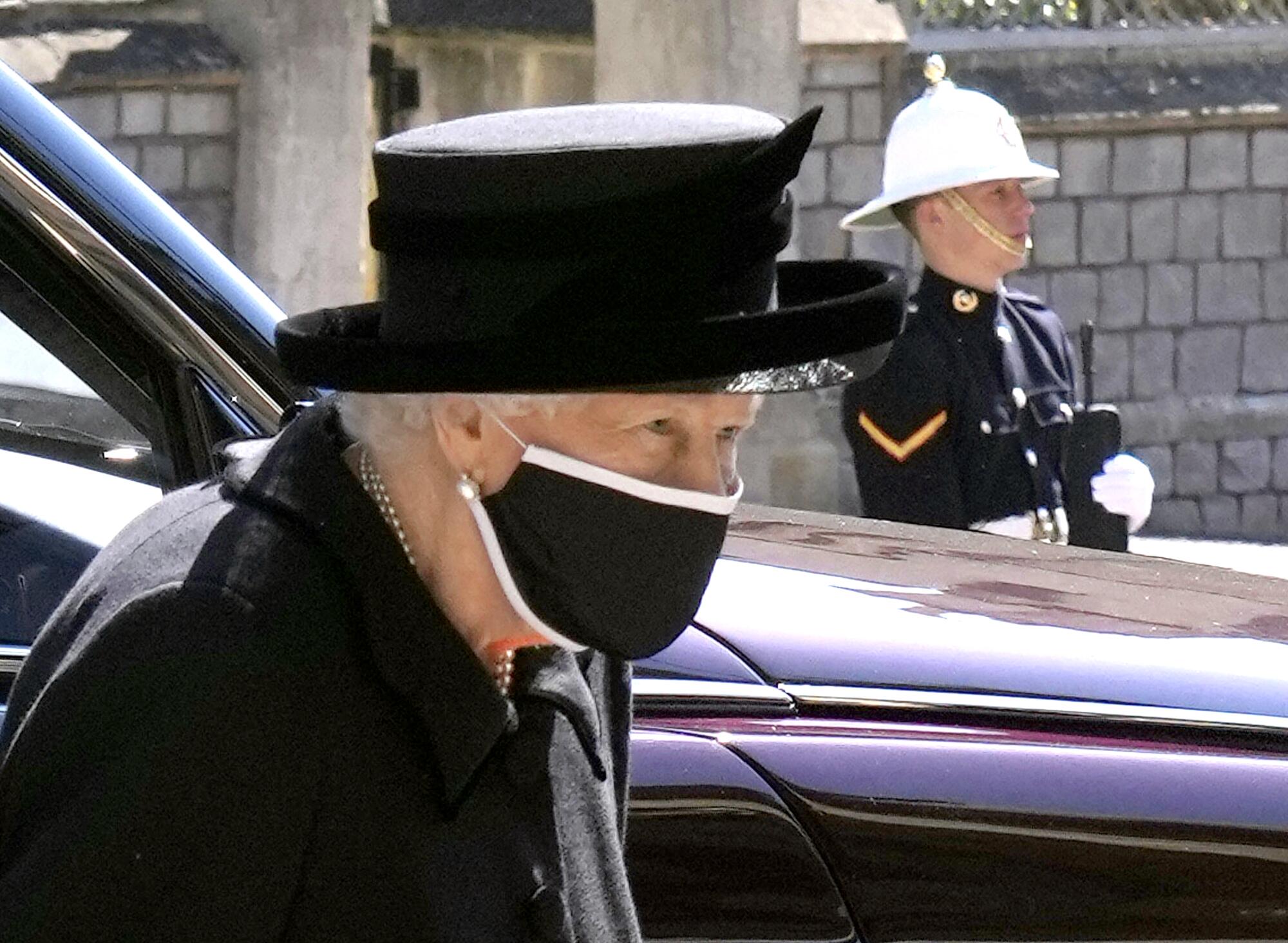 Queen Elizabeth II next to a car at Windsor Castle while a military member stands nearby.