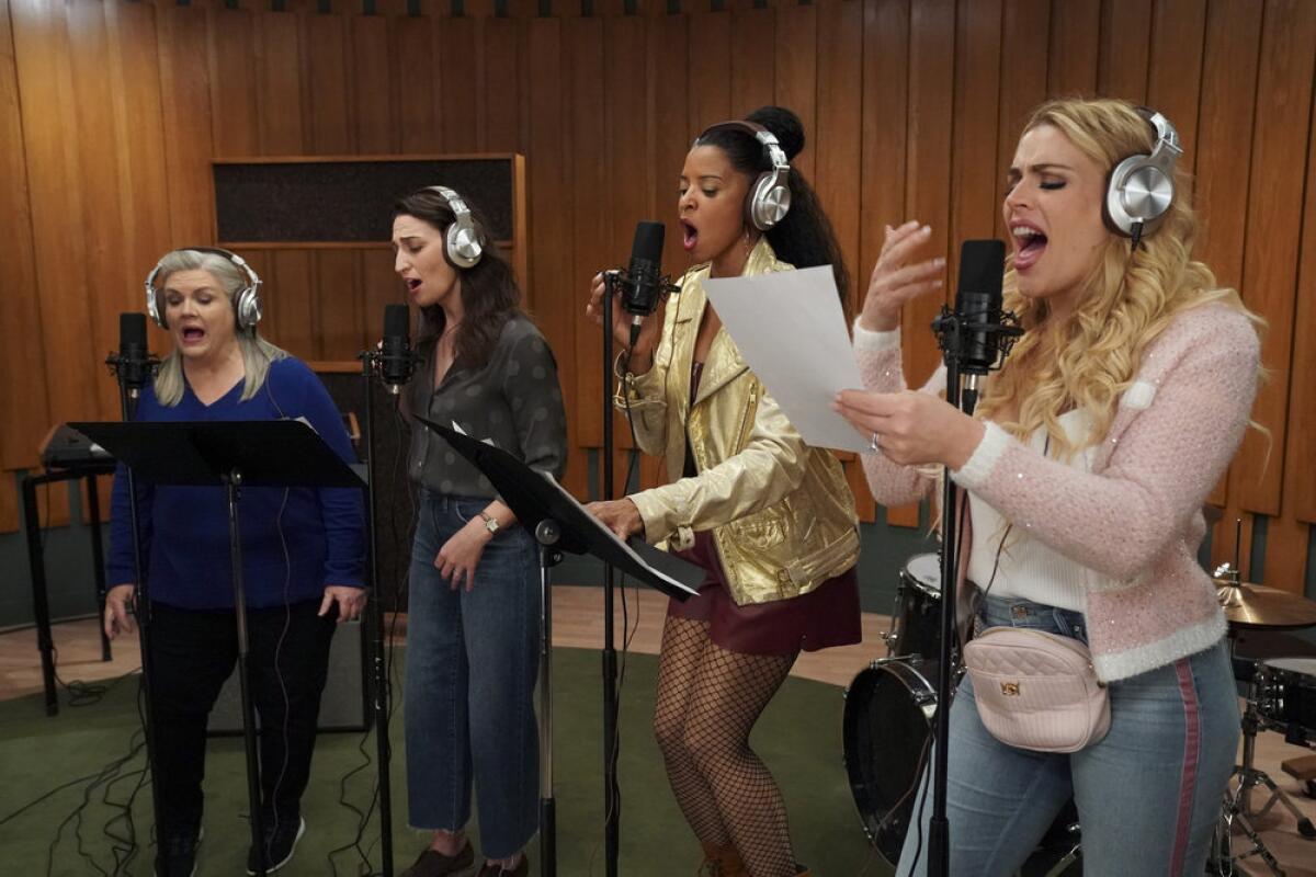 A quartet of women sings into microphones on stands in a recording studio.