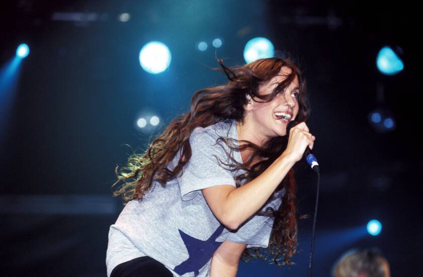 Alanis Morissette crouching and singing into a microphone