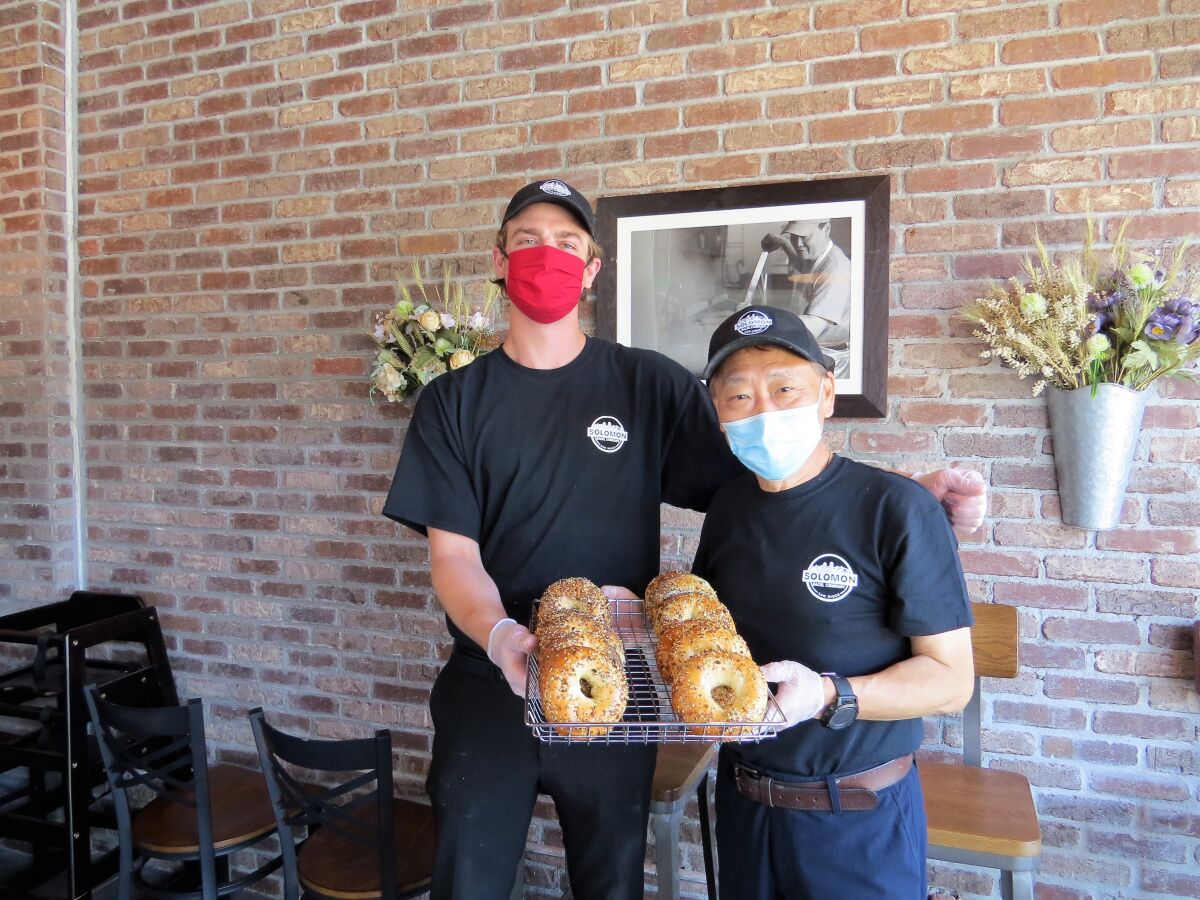 Owner Jeffrey Wang, right, and his apprentice bagel-maker Jacob Lynch hold a tray of everything bagels, the best-selling product at newly opened Solomon Bagels & Donuts in North Park on Tuesday, April 28. Despite the challenges of opening April 17, during the pandemic, the shop has been very busy.