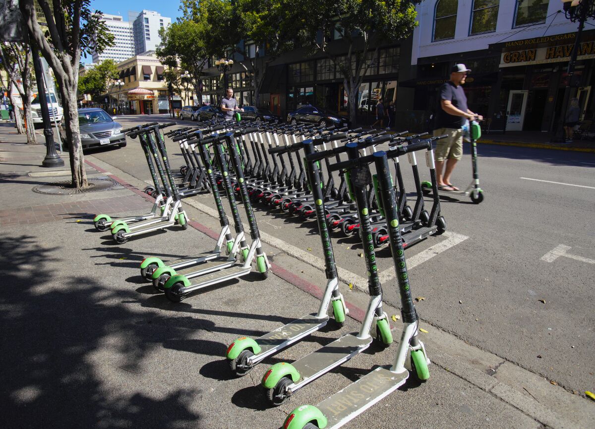 Marked corral space on 4th Avenue in downtown San Diego is packed full with scooters with nine other scooters parked just outside the corral and on sidewalk. 