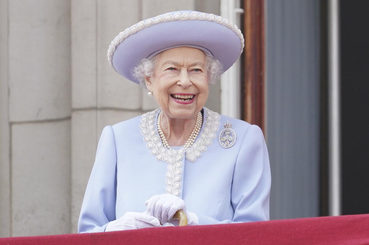 Queen Elizabeth in a lilac hat and jacket while she looks ahead smiling from her Buckingham Palace balcony