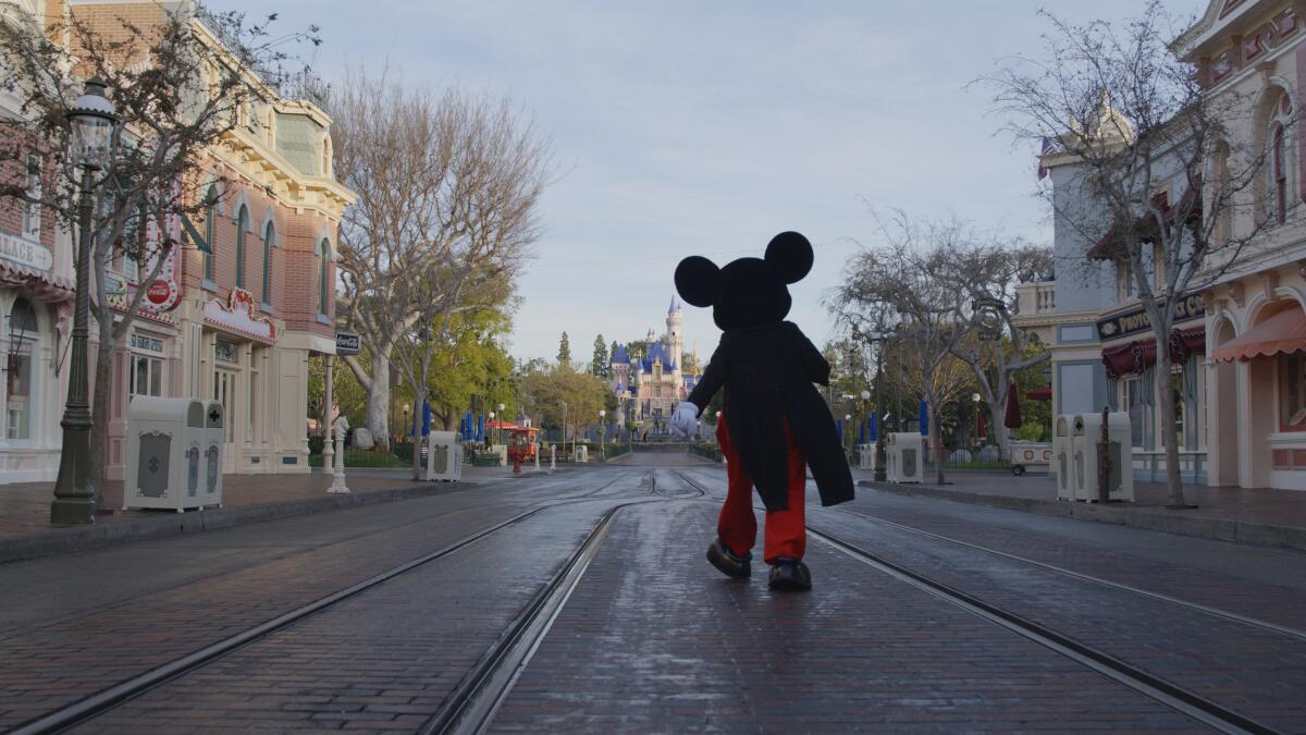 A Mickey Mouse mascot is seen from behind, walking down the street